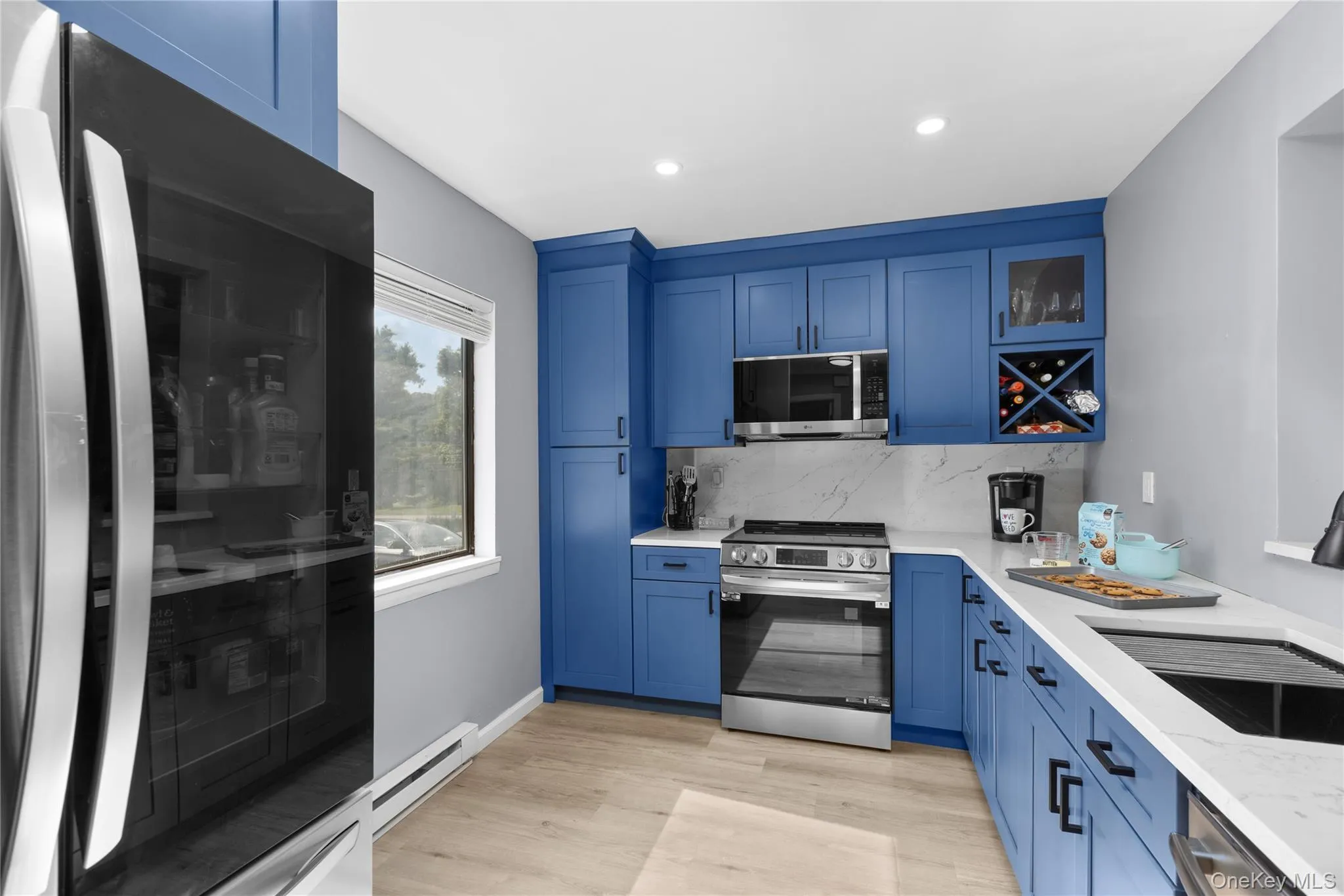 Contemporary kitchen with window that faces front of house featuring bright blue cabinetry, light vinyl flooring, recessed lighting, and stainless steel appliances Contemporary kitchen with window that faces front of house featuring bright blue cabinetry, light vinyl flooring, recessed lighting, and stainless steel appliances