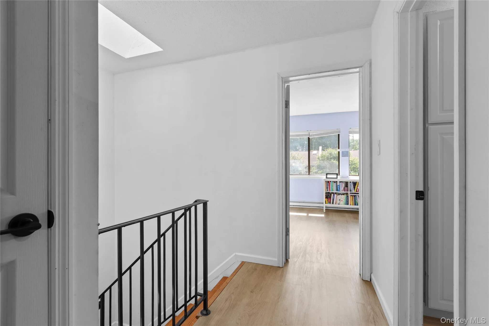 Hallway featuring light vinyl flooring, white walls, and a skylight Hallway featuring light vinyl flooring, white walls, and a skylight
