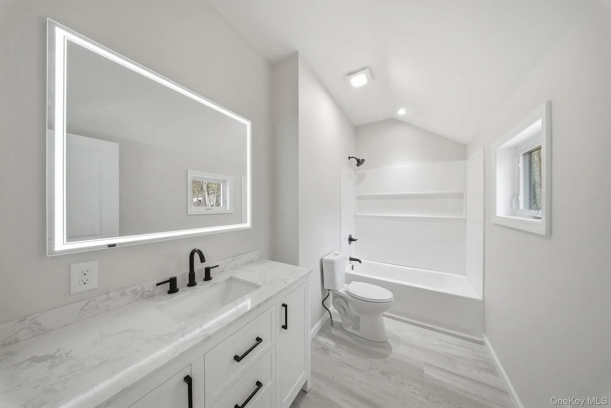 Bathroom featuring a vanity with a light-up mirror, white countertop, and dark-finish fixtures Bathroom featuring a vanity with a light-up mirror, white countertop, and dark-finish fixtures