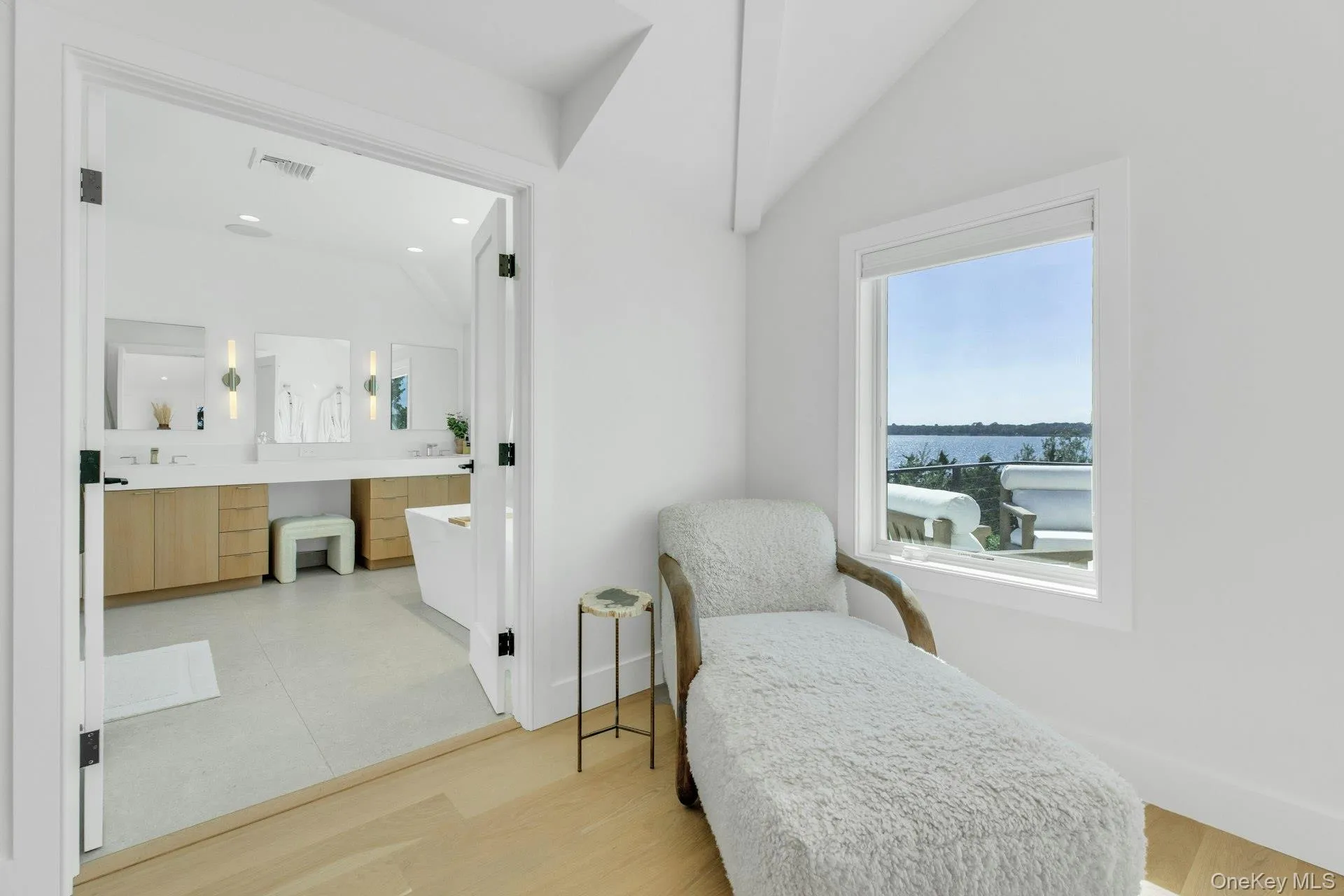 Bright interior space with light wood-finish flooring, white walls, and a window framing a water scene Bright interior space with light wood-finish flooring, white walls, and a window framing a water scene