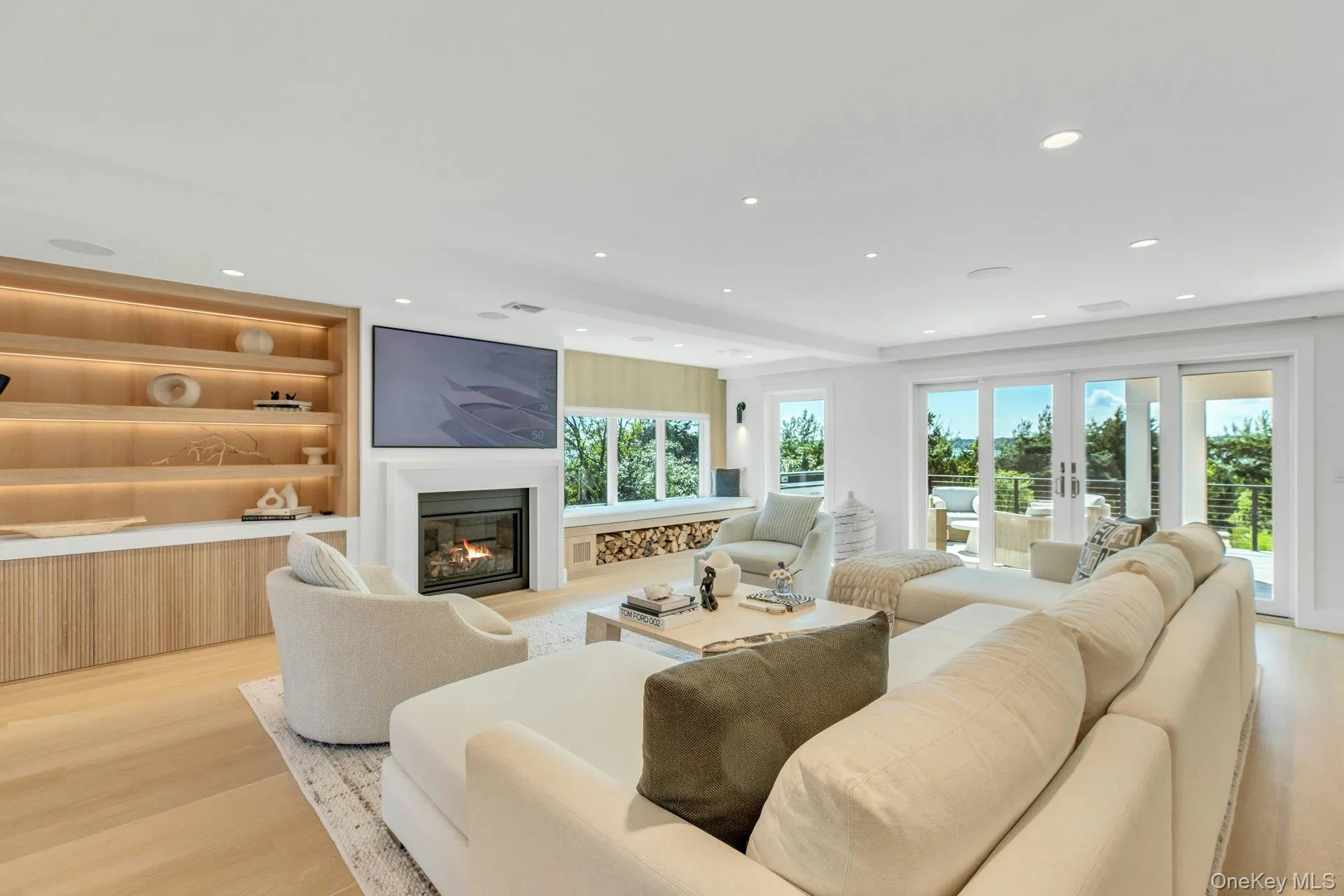 Spacious living area featuring light wood-finish flooring, recessed lighting, and a built-in entertainment center with open shelving and lower cabinetry Spacious living area featuring light wood-finish flooring, recessed lighting, and a built-in entertainment center with open shelving and lower cabinetry