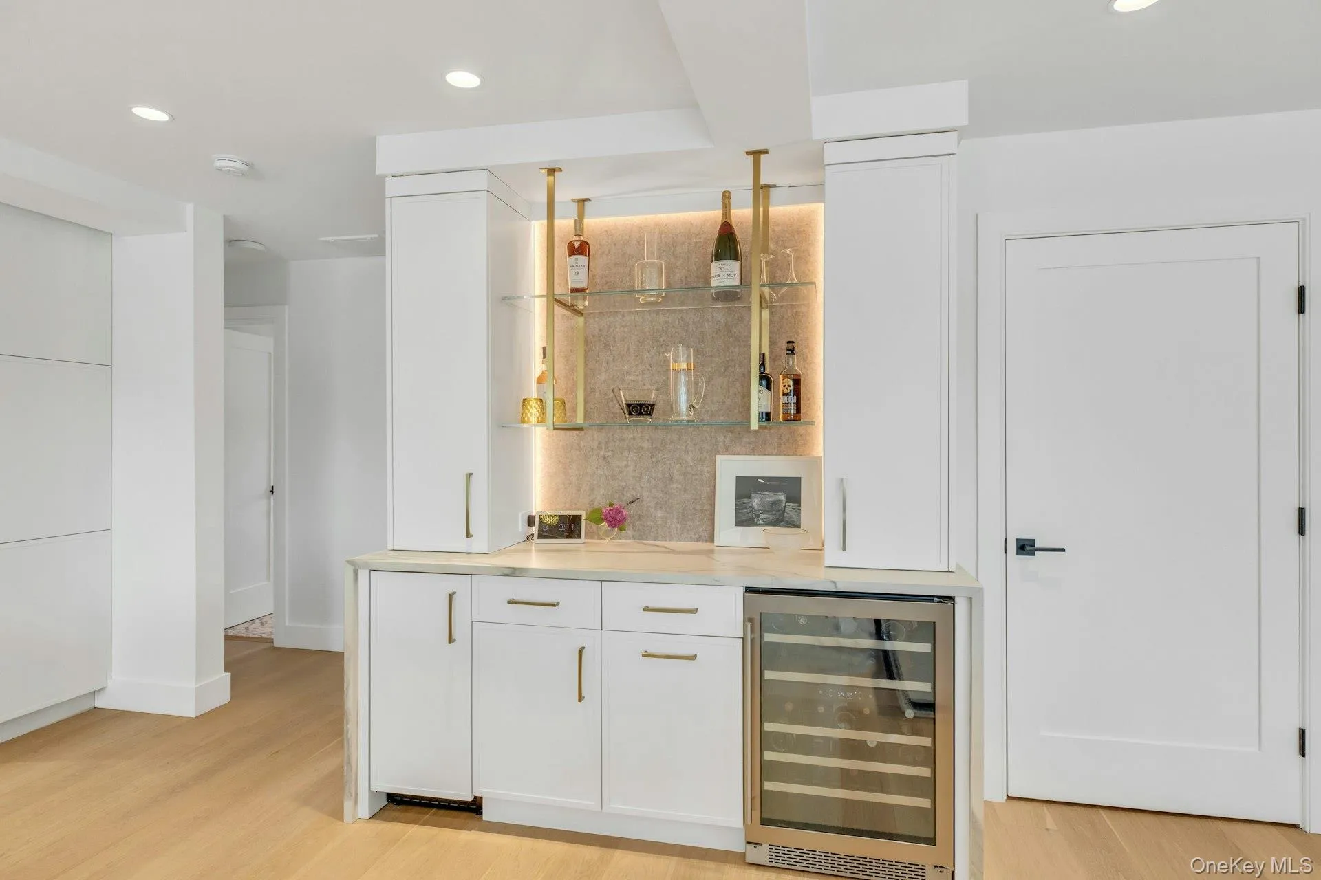 Built-in bar featuring white cabinetry, a stone countertop, a stainless steel beverage refrigerator, icemaker and open floating shelving with integrated lighting Built-in bar featuring white cabinetry, a stone countertop, a stainless steel beverage refrigerator, icemaker and open floating shelving with integrated lighting
