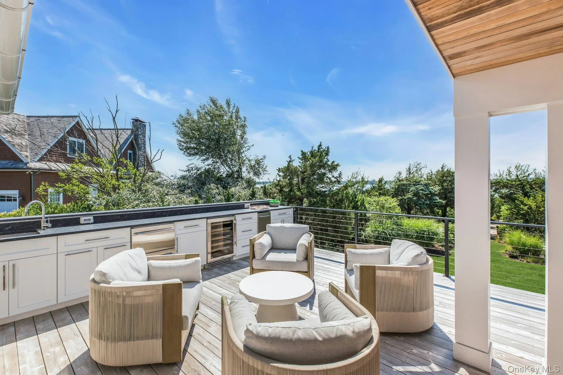 Expansive outdoor deck featuring wood-finish decking and a built-in outdoor kitchen with a sink, integrated grill, and beverage refrigerator Expansive outdoor deck featuring wood-finish decking and a built-in outdoor kitchen with a sink, integrated grill, and beverage refrigerator