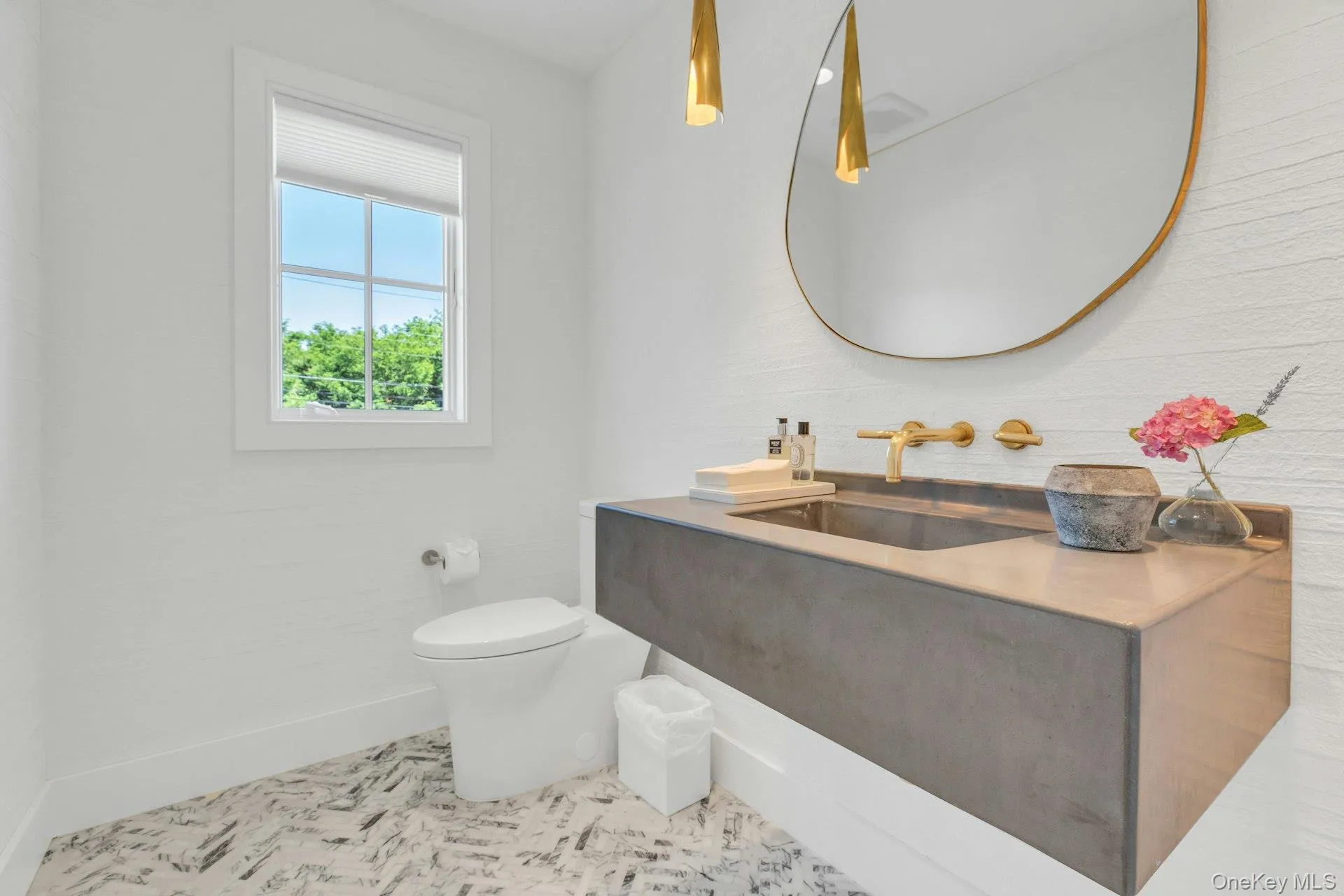 Floating vanity with integrated sink, gold-finish fixtures, and a large oval mirror Floating vanity with integrated sink, gold-finish fixtures, and a large oval mirror