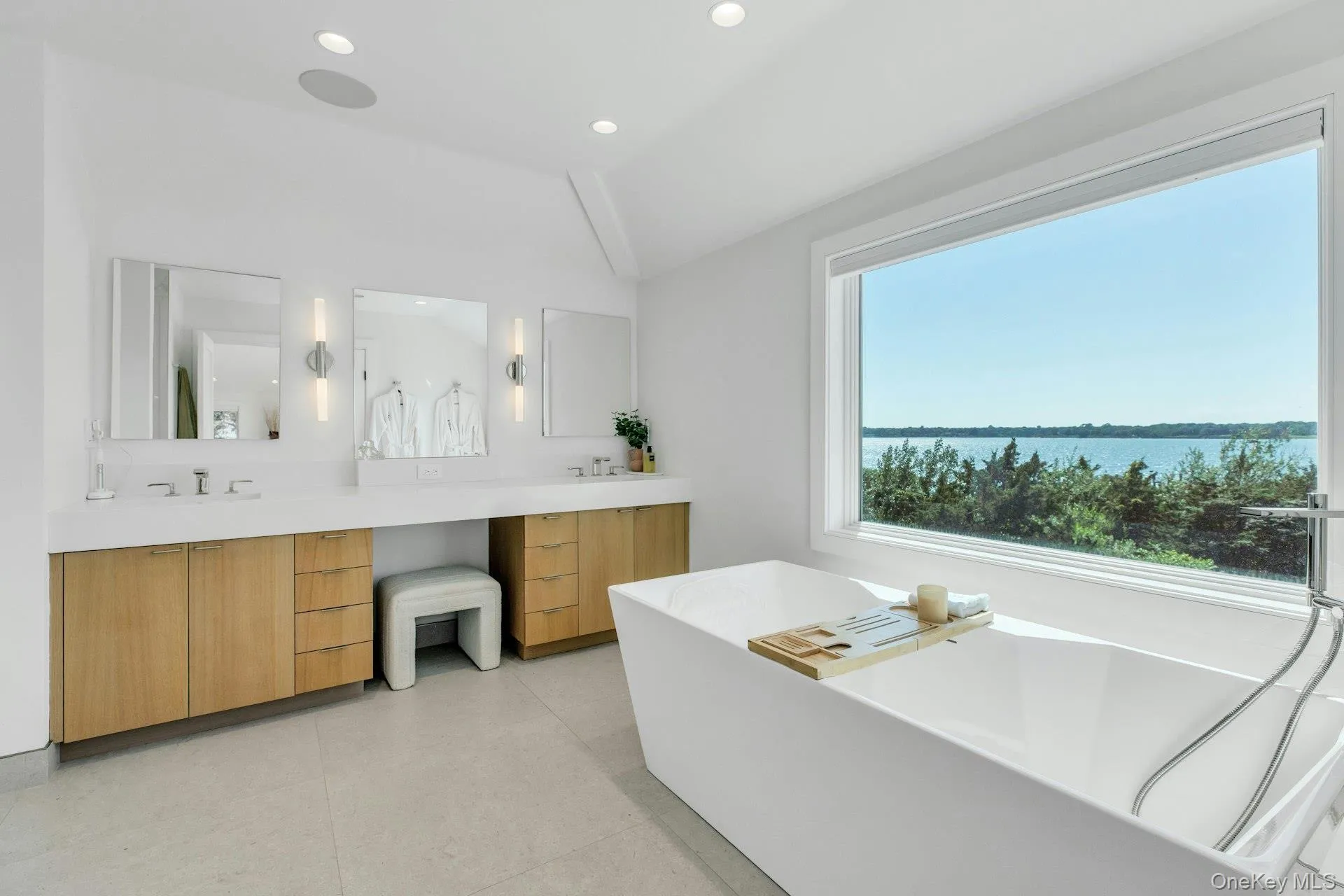 Freestanding soaking tub positioned before an expansive window overlooking a body of water and treeline Freestanding soaking tub positioned before an expansive window overlooking a body of water and treeline