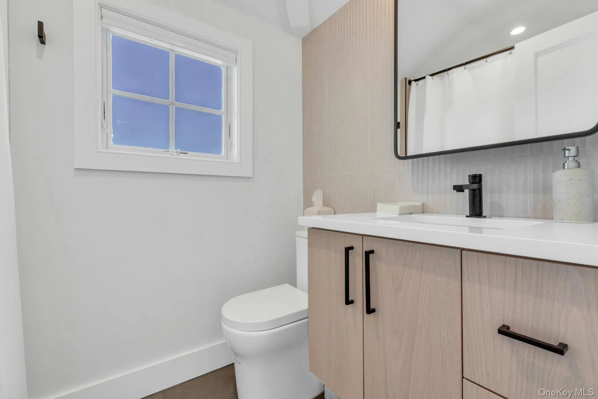 Modern bathroom featuring a wood-finish vanity with matte black hardware, white countertop, rectangular undermount sink, and a black-framed mirror Modern bathroom featuring a wood-finish vanity with matte black hardware, white countertop, rectangular undermount sink, and a black-framed mirror