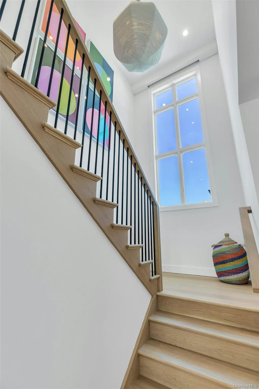 Hardwood staircase with black metal balusters and a wood-finish handrail, complemented by a tall, multi-pane window and a contemporary pendant light fixture Hardwood staircase with black metal balusters and a wood-finish handrail, complemented by a tall, multi-pane window and a contemporary pendant light fixture