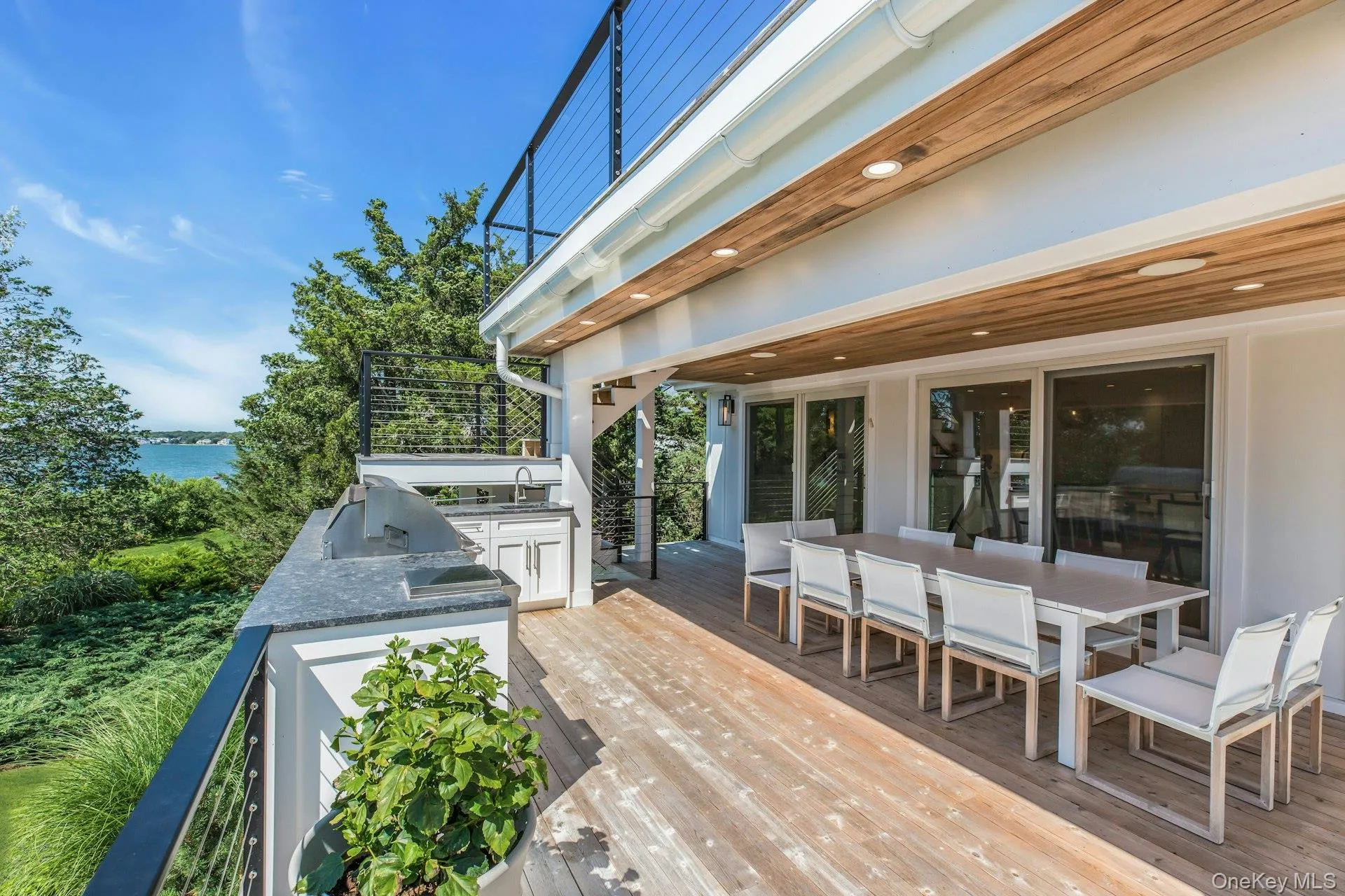 Expansive outdoor deck featuring wood-finish flooring, a built-in outdoor kitchen with grill and sink, and a cable railing system Expansive outdoor deck featuring wood-finish flooring, a built-in outdoor kitchen with grill and sink, and a cable railing system