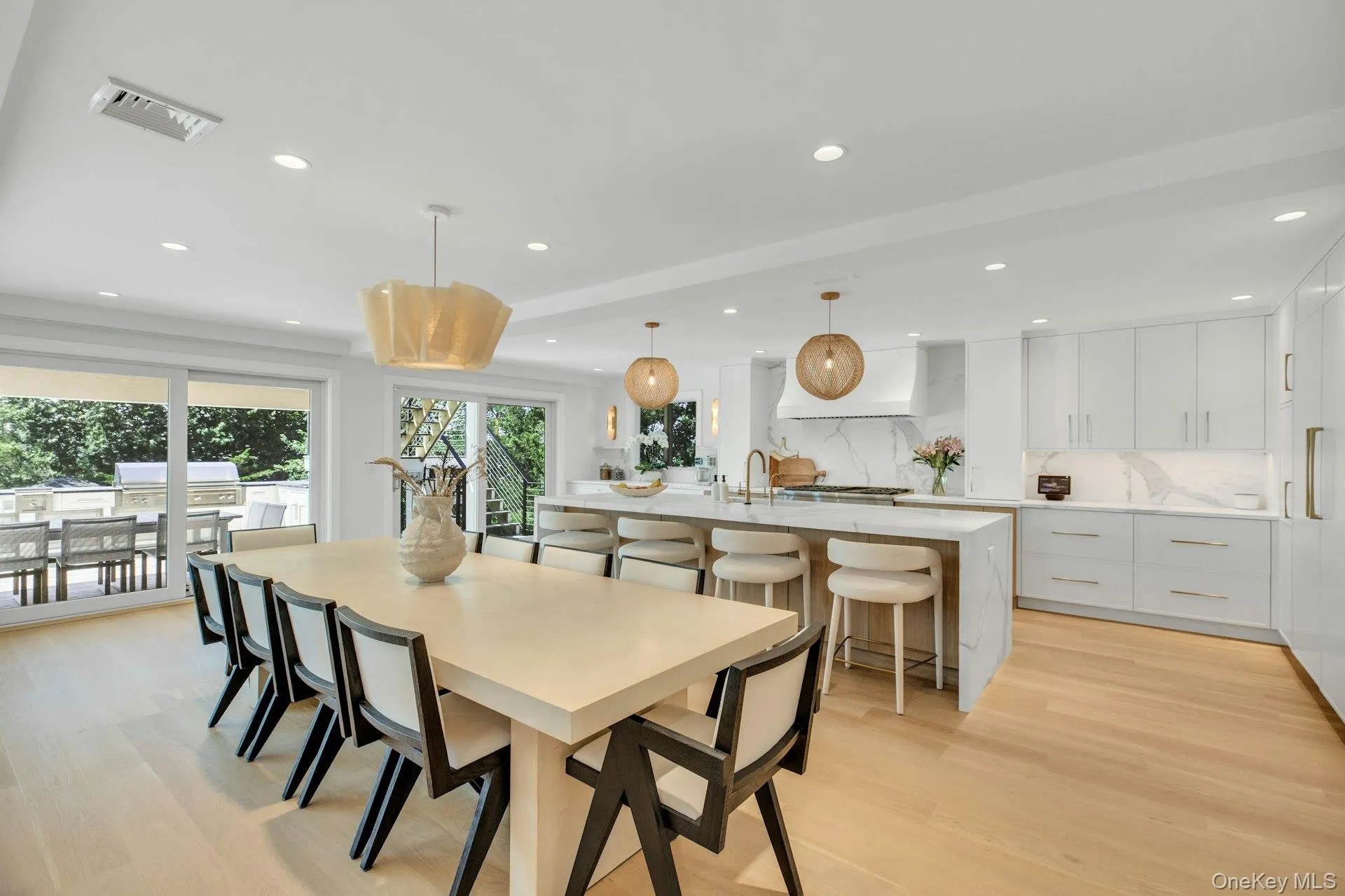 Open-concept kitchen and dining area featuring light wood-finish flooring, white cabinetry, a waterfall island, and recessed lighting Open-concept kitchen and dining area featuring light wood-finish flooring, white cabinetry, a waterfall island, and recessed lighting