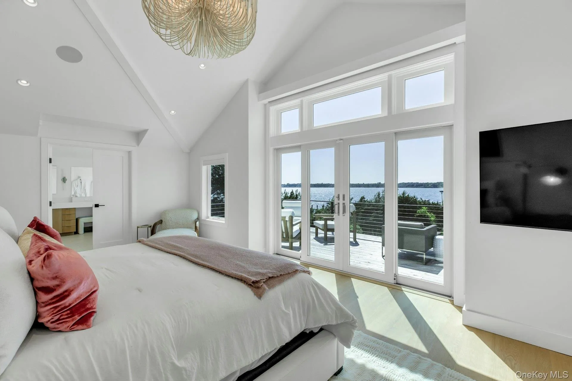 Spacious bedroom featuring vaulted ceilings, a contemporary ceiling light fixture, wood-finish flooring, and a sliding glass door leading to an outdoor deck Spacious bedroom featuring vaulted ceilings, a contemporary ceiling light fixture, wood-finish flooring, and a sliding glass door leading to an outdoor deck