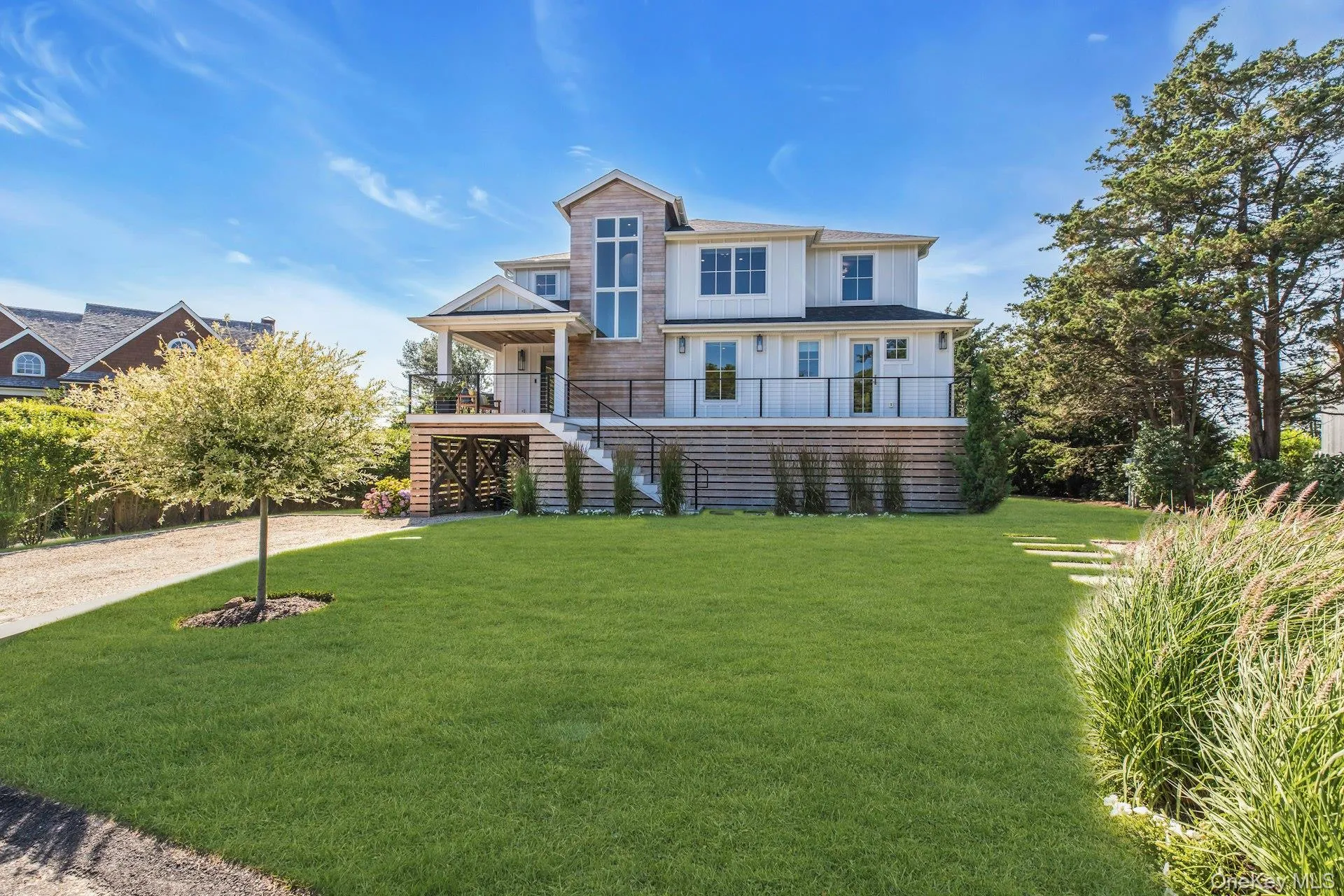 Custom coastal residence featuring board and batten siding, natural wood shingle accents, multiple balconies with black railings, and an expansive front lawn Custom coastal residence featuring board and batten siding, natural wood shingle accents, multiple balconies with black railings, and an expansive front lawn