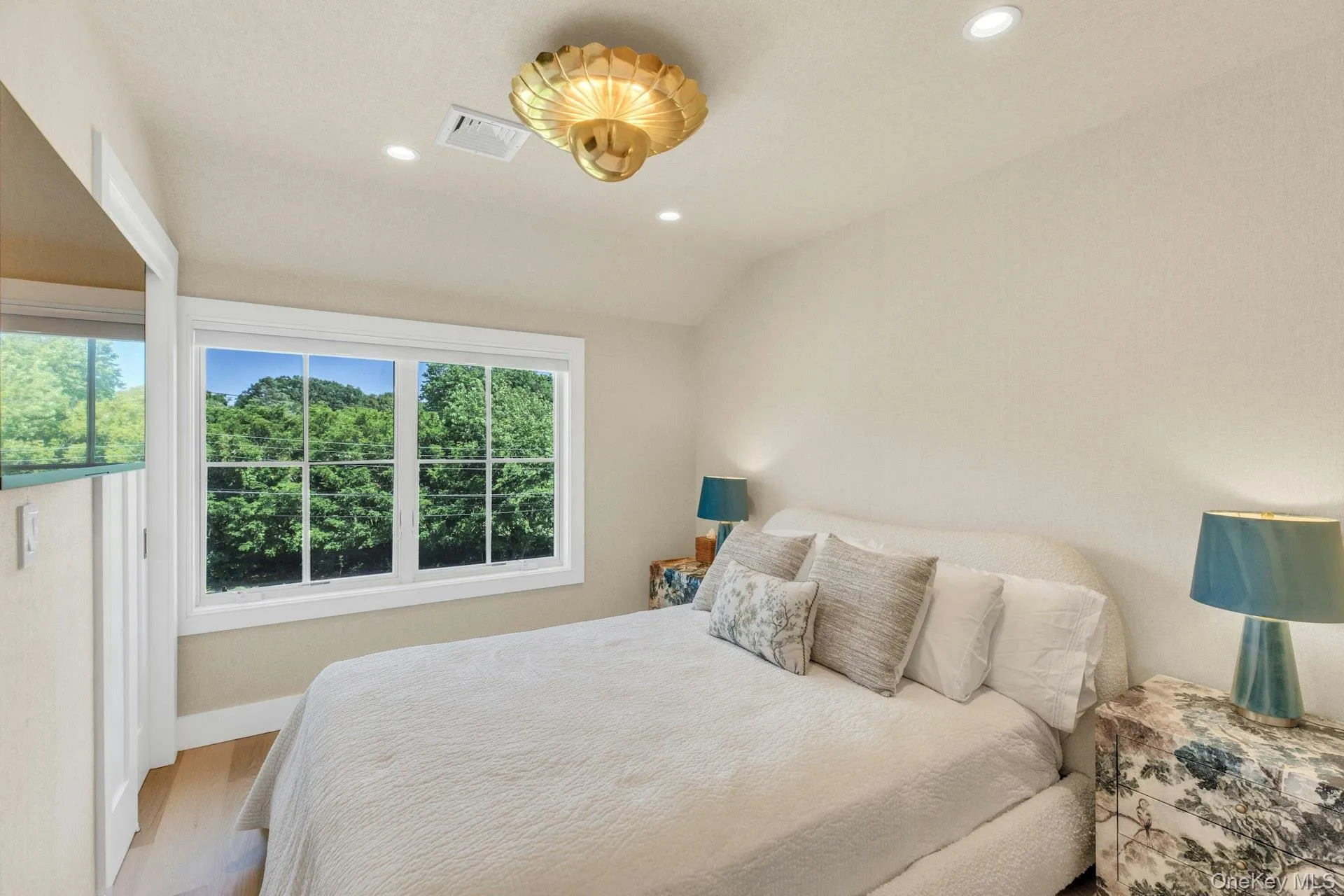 Spacious room featuring a multi-pane window with white trim, wood-finish flooring, a textured wall finish, recessed lighting, and a decorative gold-toned ceiling fixture Spacious room featuring a multi-pane window with white trim, wood-finish flooring, a textured wall finish, recessed lighting, and a decorative gold-toned ceiling fixture