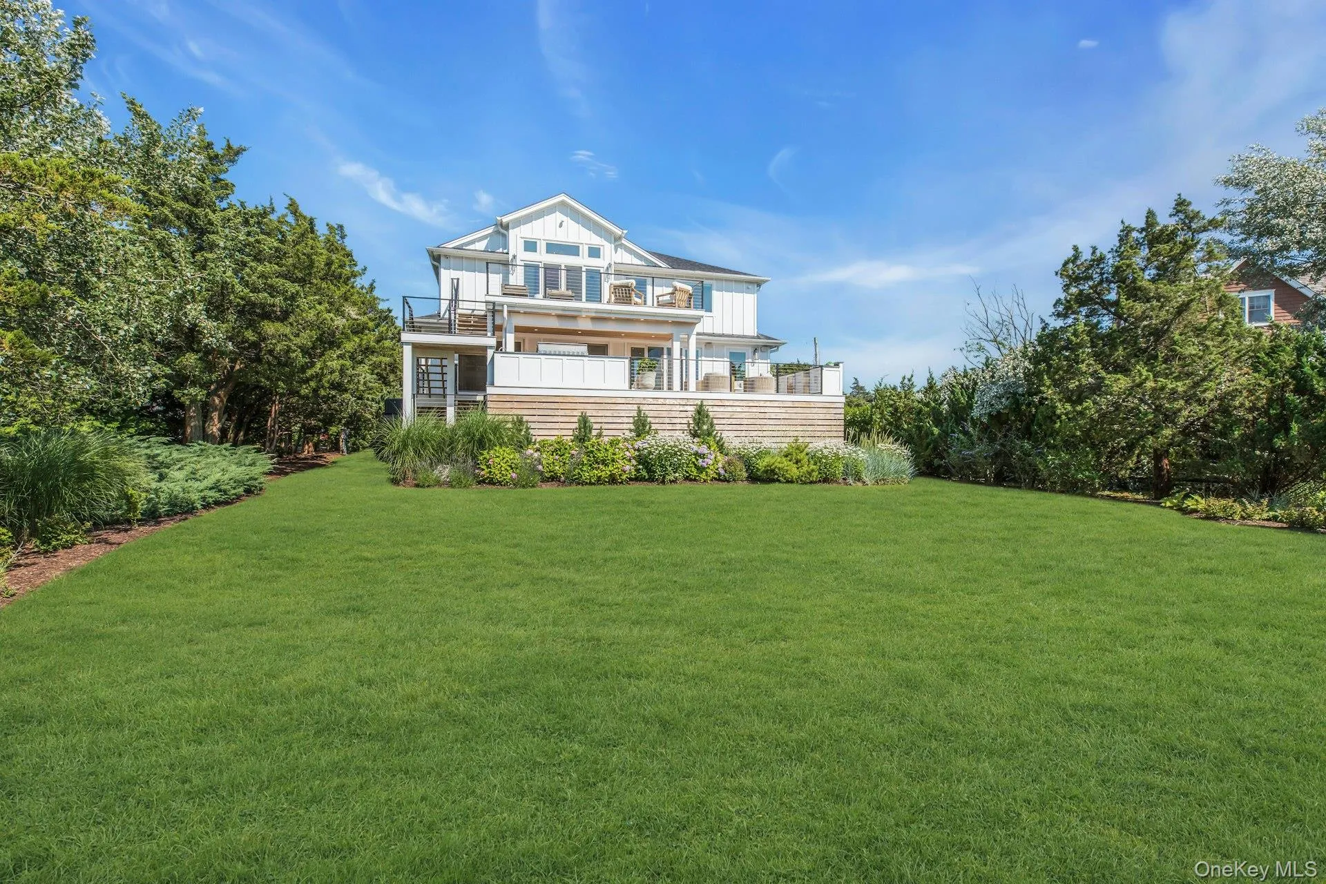 Expansive green lawn bordering a multi-level deck and white shiplap exterior Expansive green lawn bordering a multi-level deck and white shiplap exterior