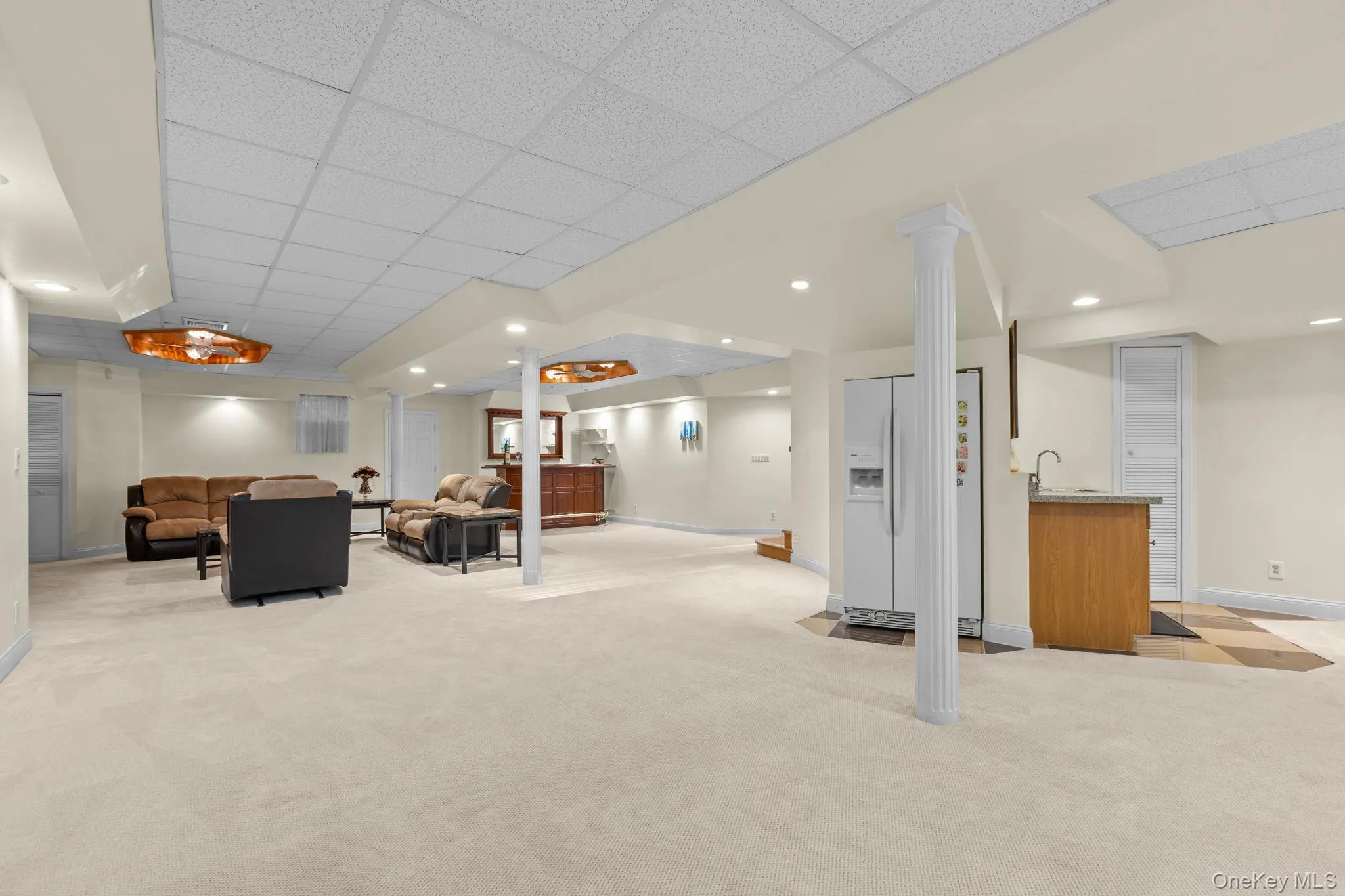 Designed for effortless entertaining, this expansive recreation space features a refrigerator, cabinetry with sink, and high ceilings, creating a versatile gathering area Designed for effortless entertaining, this expansive recreation space features a refrigerator, cabinetry with sink, and high ceilings, creating a versatile gathering area