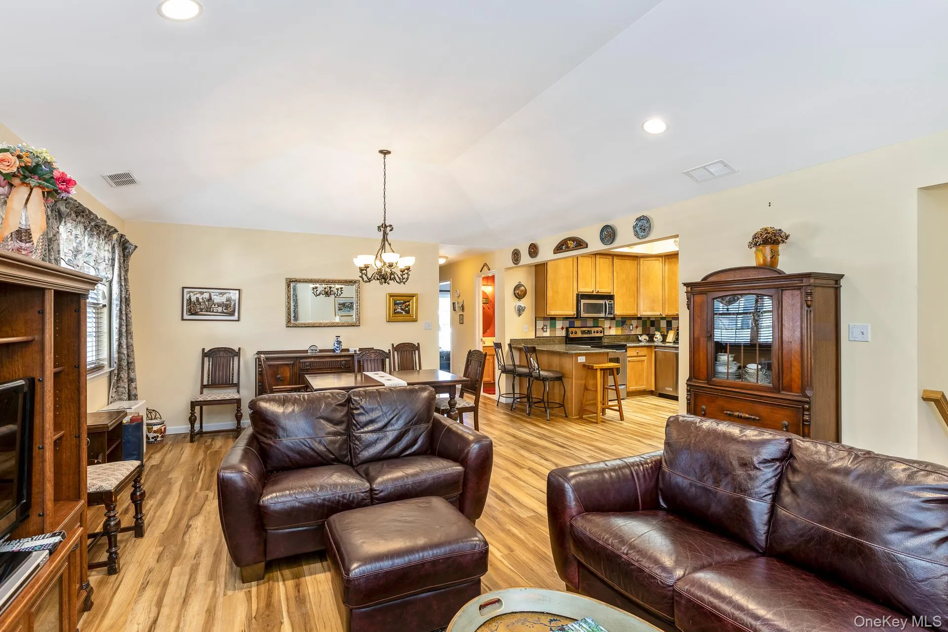 Open-concept living space featuring wood-finish flooring, a vaulted ceiling with recessed lighting, and a dining area with a chandelier Open-concept living space featuring wood-finish flooring, a vaulted ceiling with recessed lighting, and a dining area with a chandelier