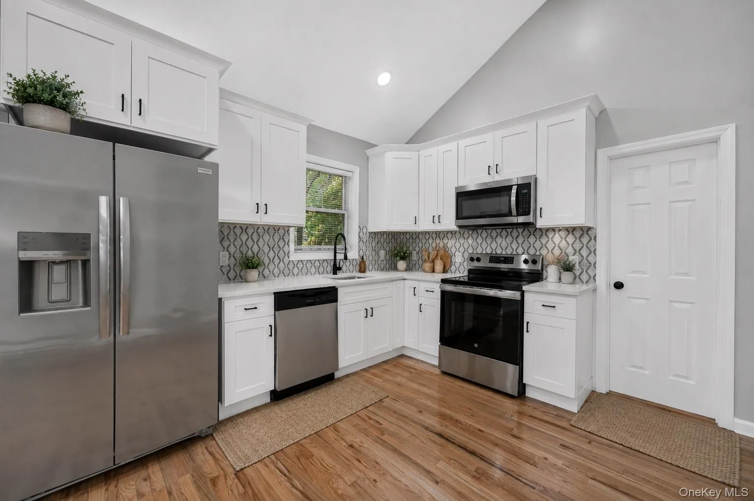 Kitchen featuring white cabinetry, stainless steel appliances, patterned tile backsplash, light countertops, and wood-finish flooring Kitchen featuring white cabinetry, stainless steel appliances, patterned tile backsplash, light countertops, and wood-finish flooring