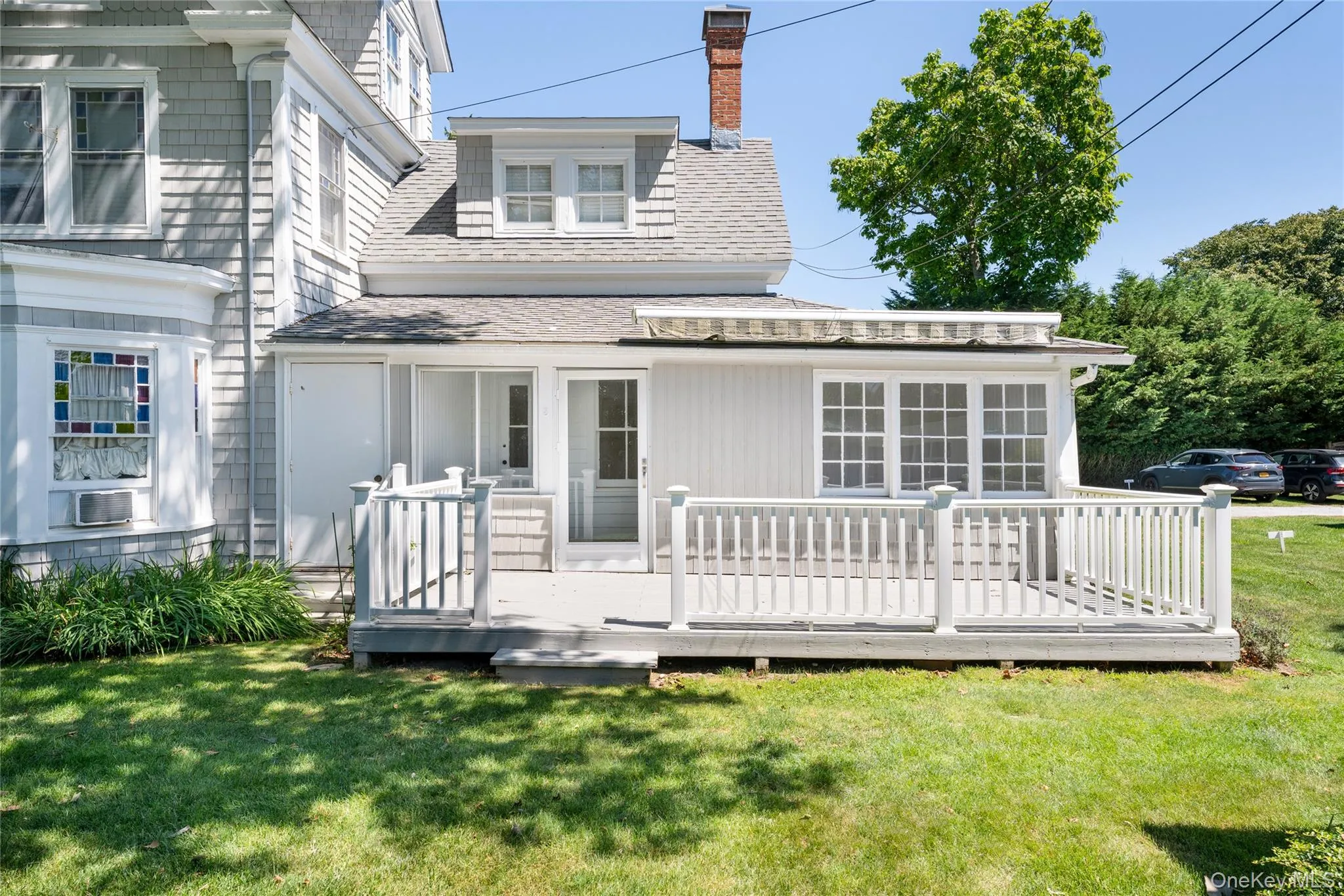 Rear view of property with a chimney, roof with shingles, a lawn, and a wooden deck Rear view of property with a chimney, roof with shingles, a lawn, and a wooden deck