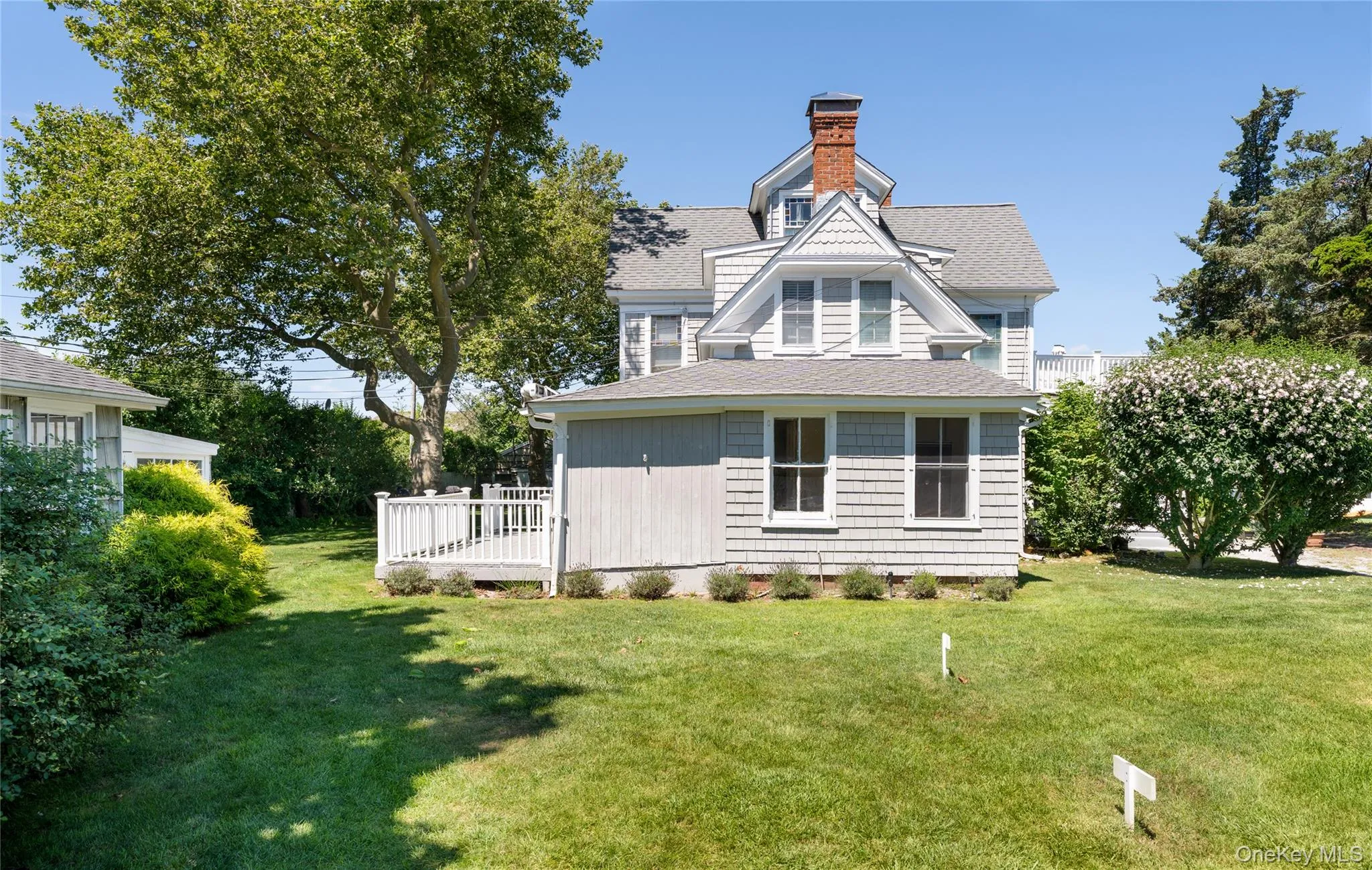 Rear view of house with a shingled roof, a lawn, a chimney, and a deck Rear view of house with a shingled roof, a lawn, a chimney, and a deck