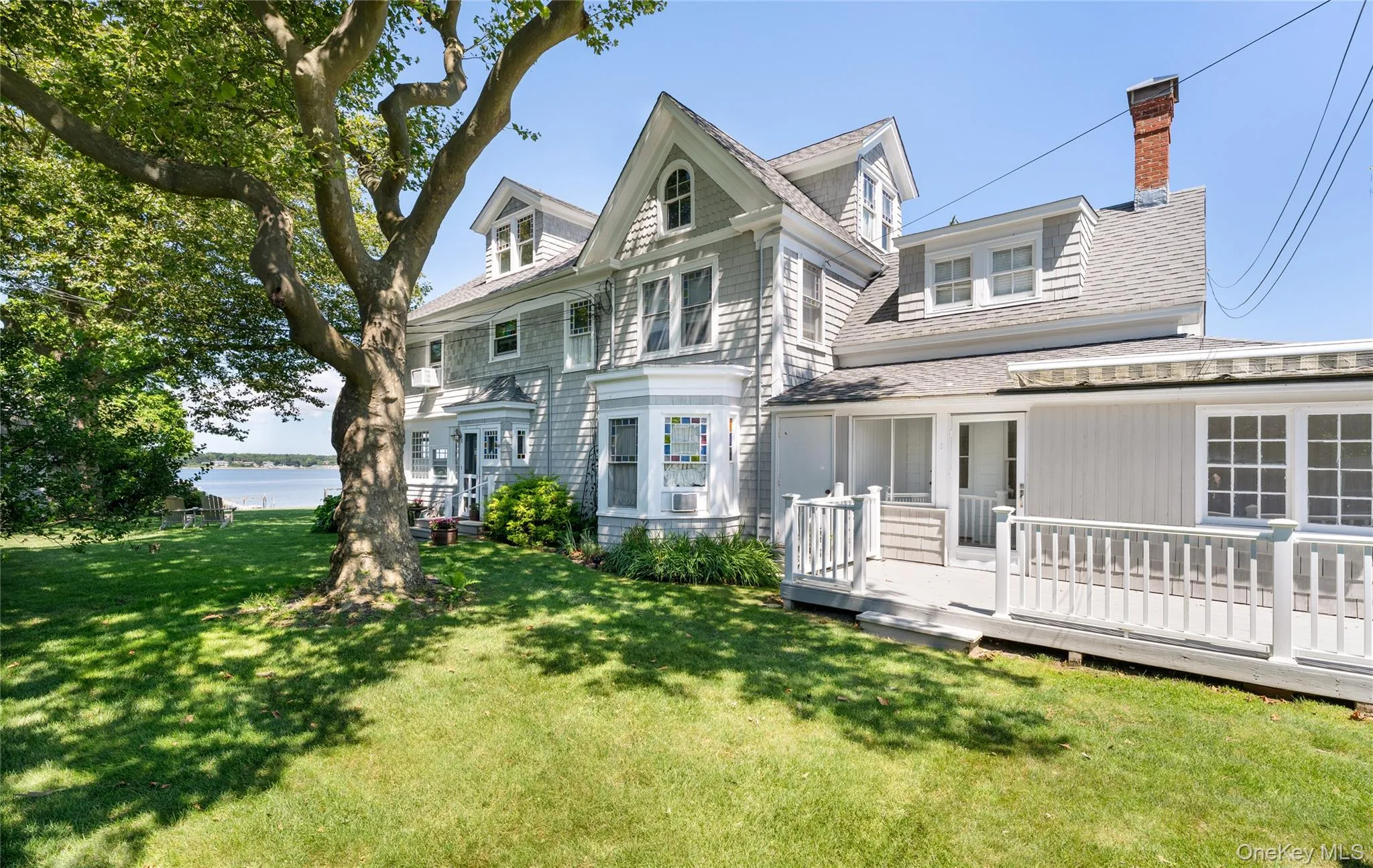 View of front facade with a front yard, a chimney, and a deck with water view View of front facade with a front yard, a chimney, and a deck with water view