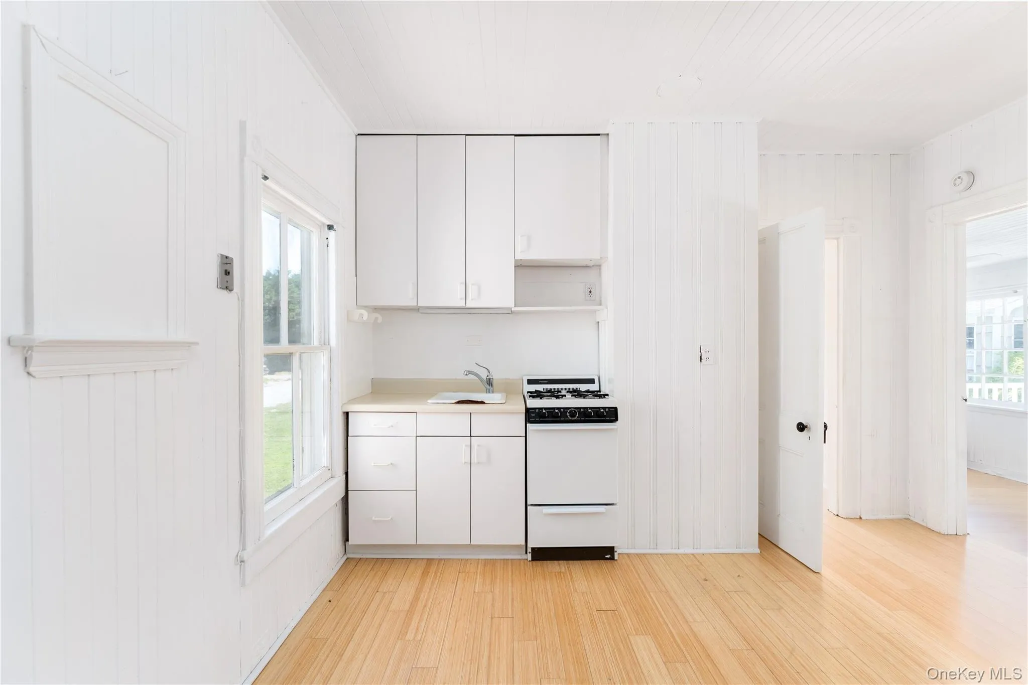 Kitchen with white range with gas cooktop, light wood finished floors, white cabinets, and plenty of natural light Kitchen with white range with gas cooktop, light wood finished floors, white cabinets, and plenty of natural light