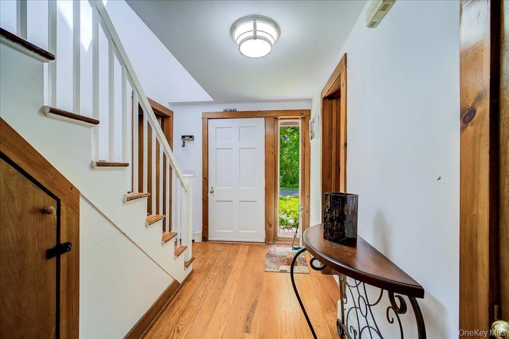 Foyer featuring wood-finish flooring, a white paneled entry door with sidelight, natural wood trim, and a staircase with white risers and wood treads Foyer featuring wood-finish flooring, a white paneled entry door with sidelight, natural wood trim, and a staircase with white risers and wood treads