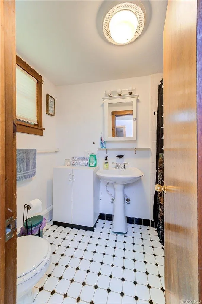 Bathroom featuring a black and white tiled floor, a white pedestal sink, a white medicine cabinet, a white storage cabinet, and a window with blinds Bathroom featuring a black and white tiled floor, a white pedestal sink, a white medicine cabinet, a white storage cabinet, and a window with blinds