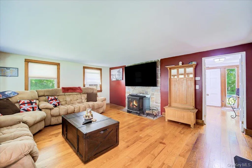 Living area featuring wood-finish flooring, a stone accent wall with a built-in wood stove, and natural wood trim around windows and doorways Living area featuring wood-finish flooring, a stone accent wall with a built-in wood stove, and natural wood trim around windows and doorways