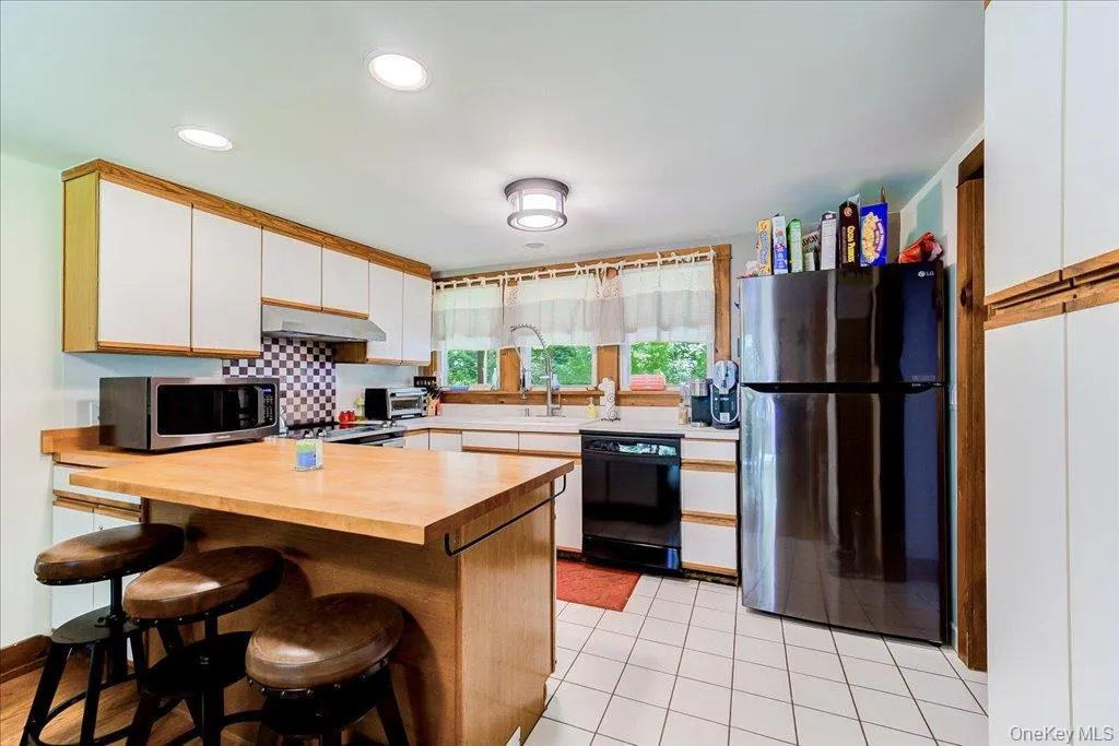 Kitchen featuring a wood-finish island with counter seating, white cabinetry with wood trim, white countertops, tile flooring, and a stainless steel range hood Kitchen featuring a wood-finish island with counter seating, white cabinetry with wood trim, white countertops, tile flooring, and a stainless steel range hood