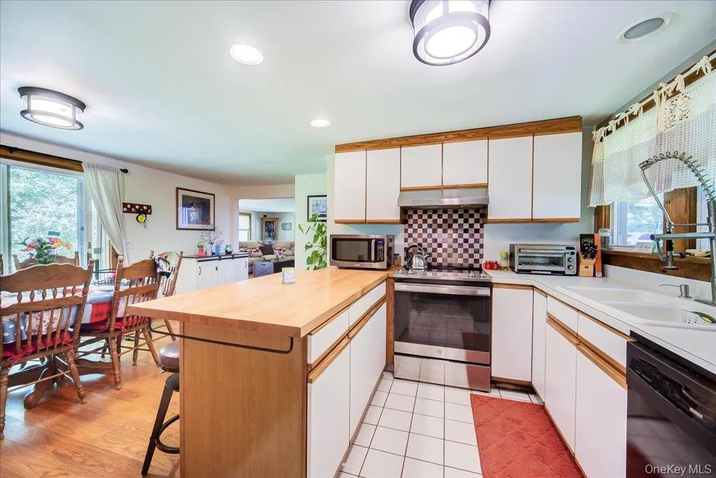 Kitchen featuring white cabinetry, light wood-finish countertops, stainless steel appliances, and a checkerboard tile backsplash Kitchen featuring white cabinetry, light wood-finish countertops, stainless steel appliances, and a checkerboard tile backsplash