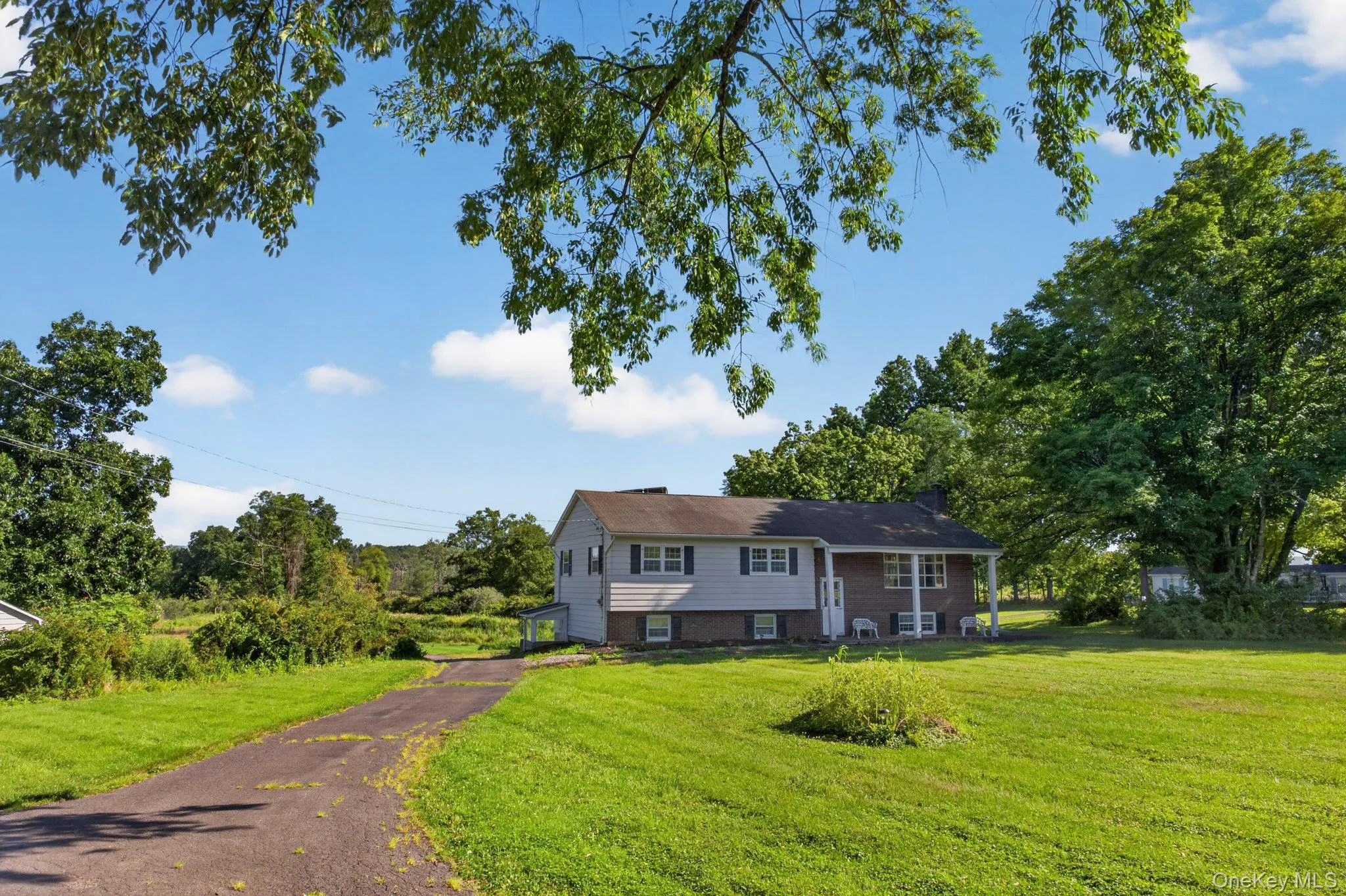 Ranch-style residence featuring a brick and siding exterior, a covered front porch, and a paved driveway Ranch-style residence featuring a brick and siding exterior, a covered front porch, and a paved driveway