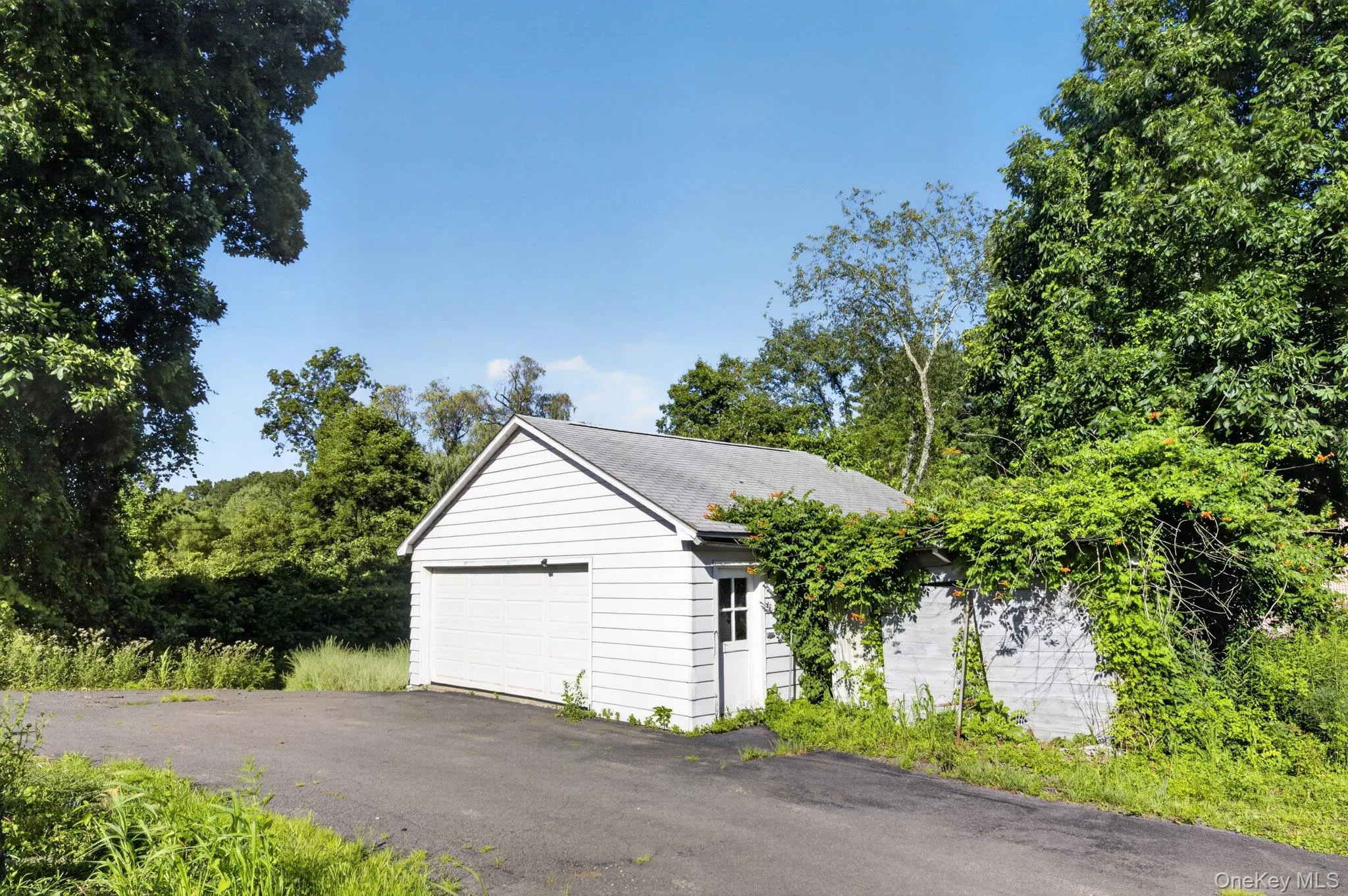 Detached garage with white siding, a single overhead door, and an exterior side door Detached garage with white siding, a single overhead door, and an exterior side door