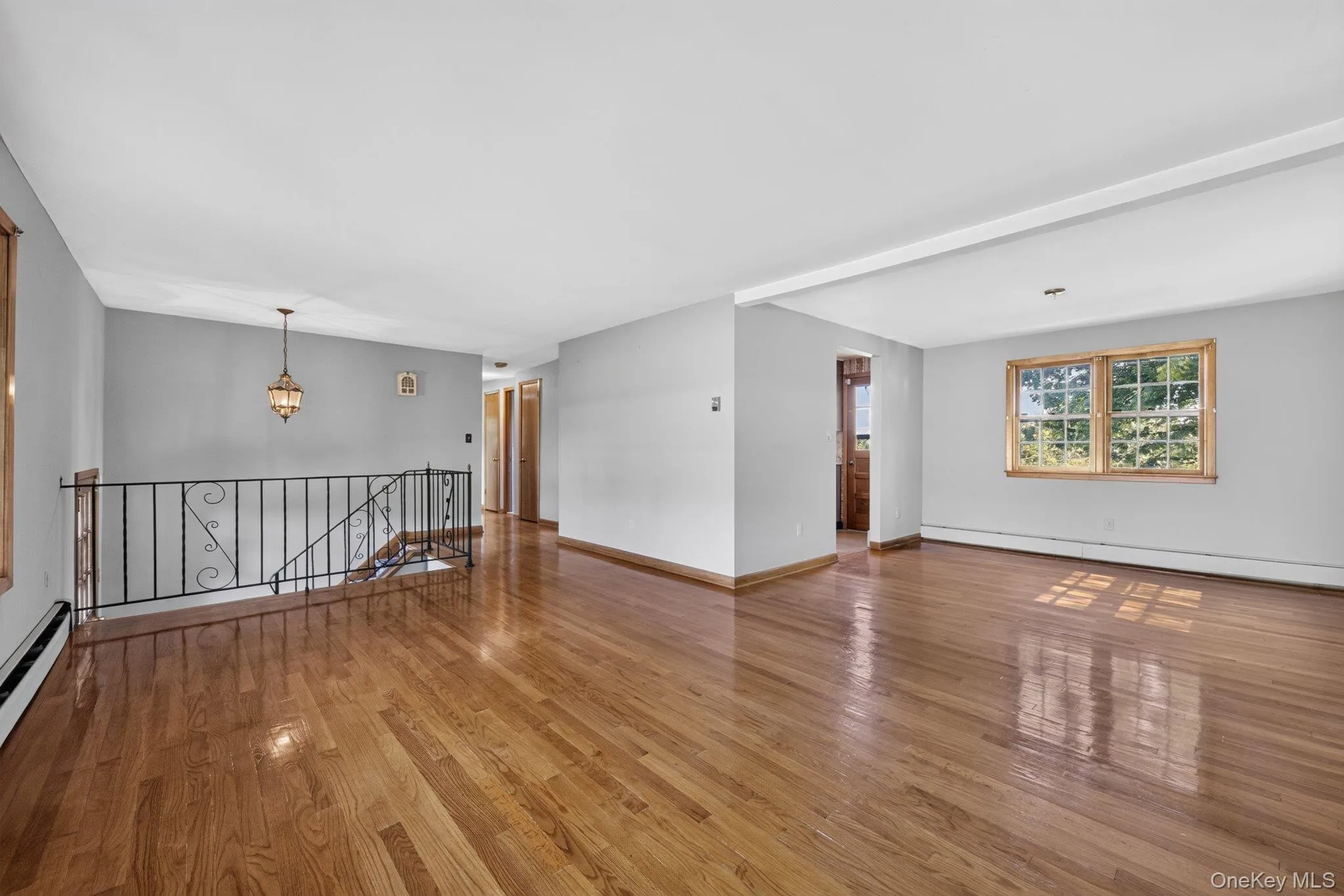 Spacious room with wood-finish flooring, light grey walls, and ample natural light from a multi-pane window Spacious room with wood-finish flooring, light grey walls, and ample natural light from a multi-pane window