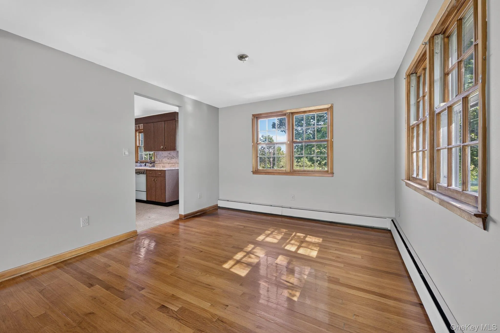Spacious room featuring wood-finish flooring, light grey painted walls, and natural wood window frames Spacious room featuring wood-finish flooring, light grey painted walls, and natural wood window frames