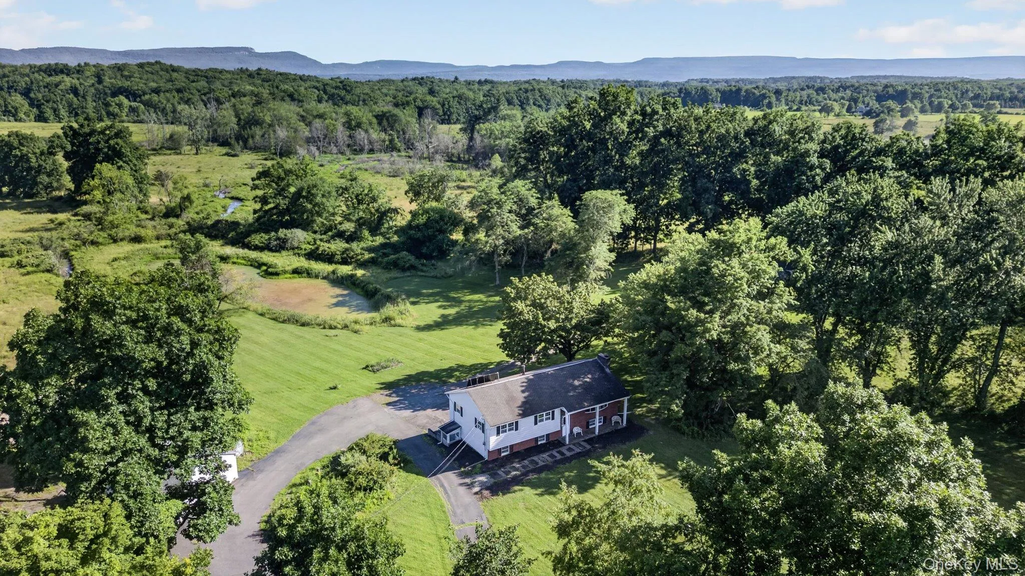 Expansive property featuring a white two-story residence with a dark roof, surrounded by mature trees, and a paved driveway Expansive property featuring a white two-story residence with a dark roof, surrounded by mature trees, and a paved driveway