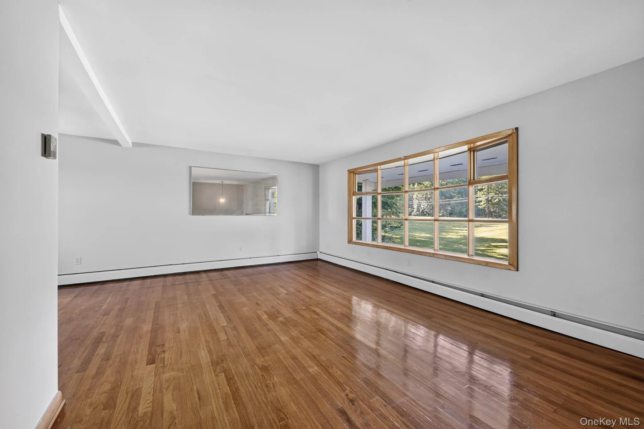 Spacious interior featuring wood-finish flooring, white walls, and a large multi-pane window with wood trim Spacious interior featuring wood-finish flooring, white walls, and a large multi-pane window with wood trim