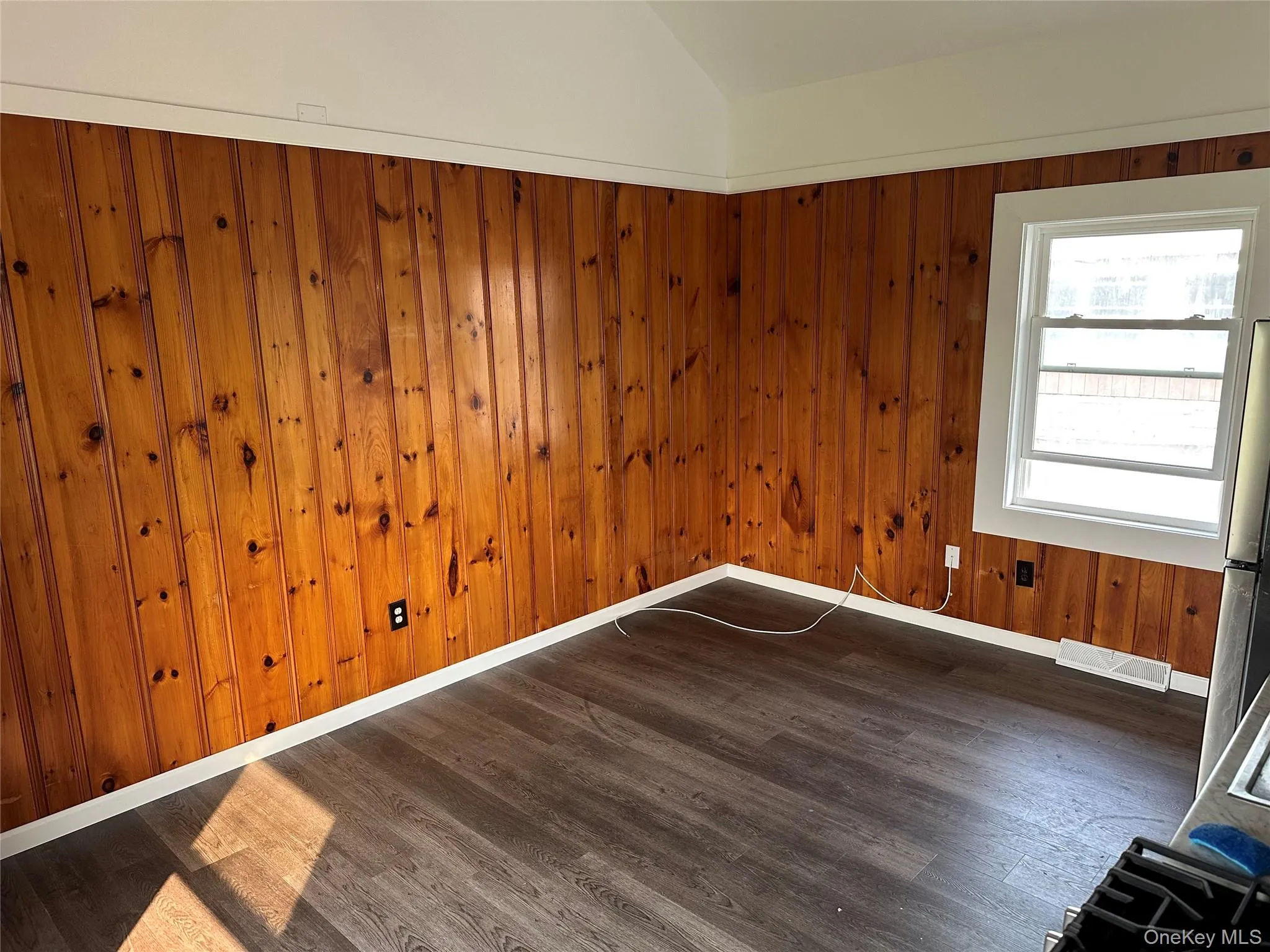 Room featuring wood paneling, wood-finish flooring, and a white trim window Room featuring wood paneling, wood-finish flooring, and a white trim window