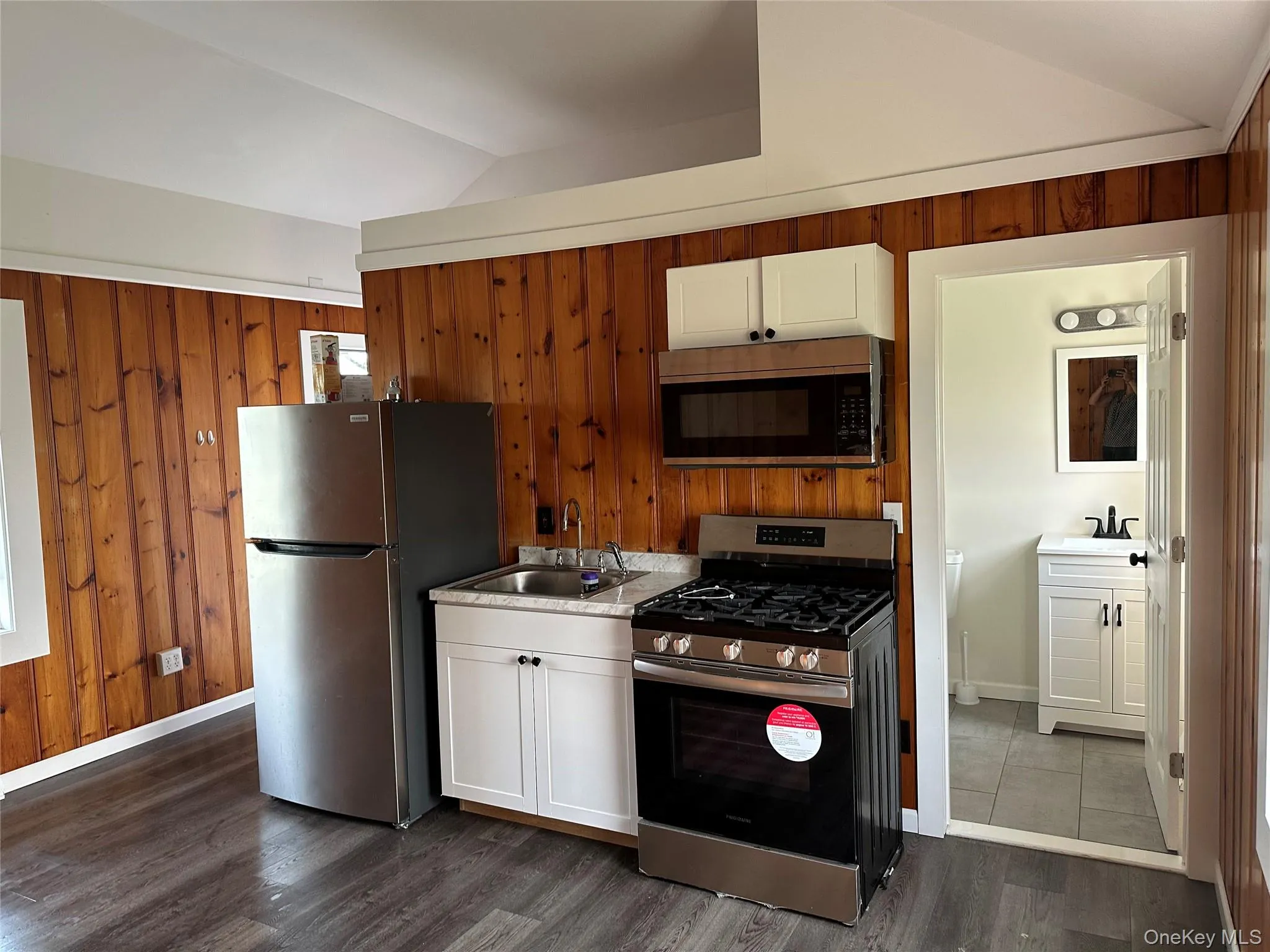 Compact kitchen featuring stainless steel appliances, white cabinetry, and wood-finish flooring Compact kitchen featuring stainless steel appliances, white cabinetry, and wood-finish flooring