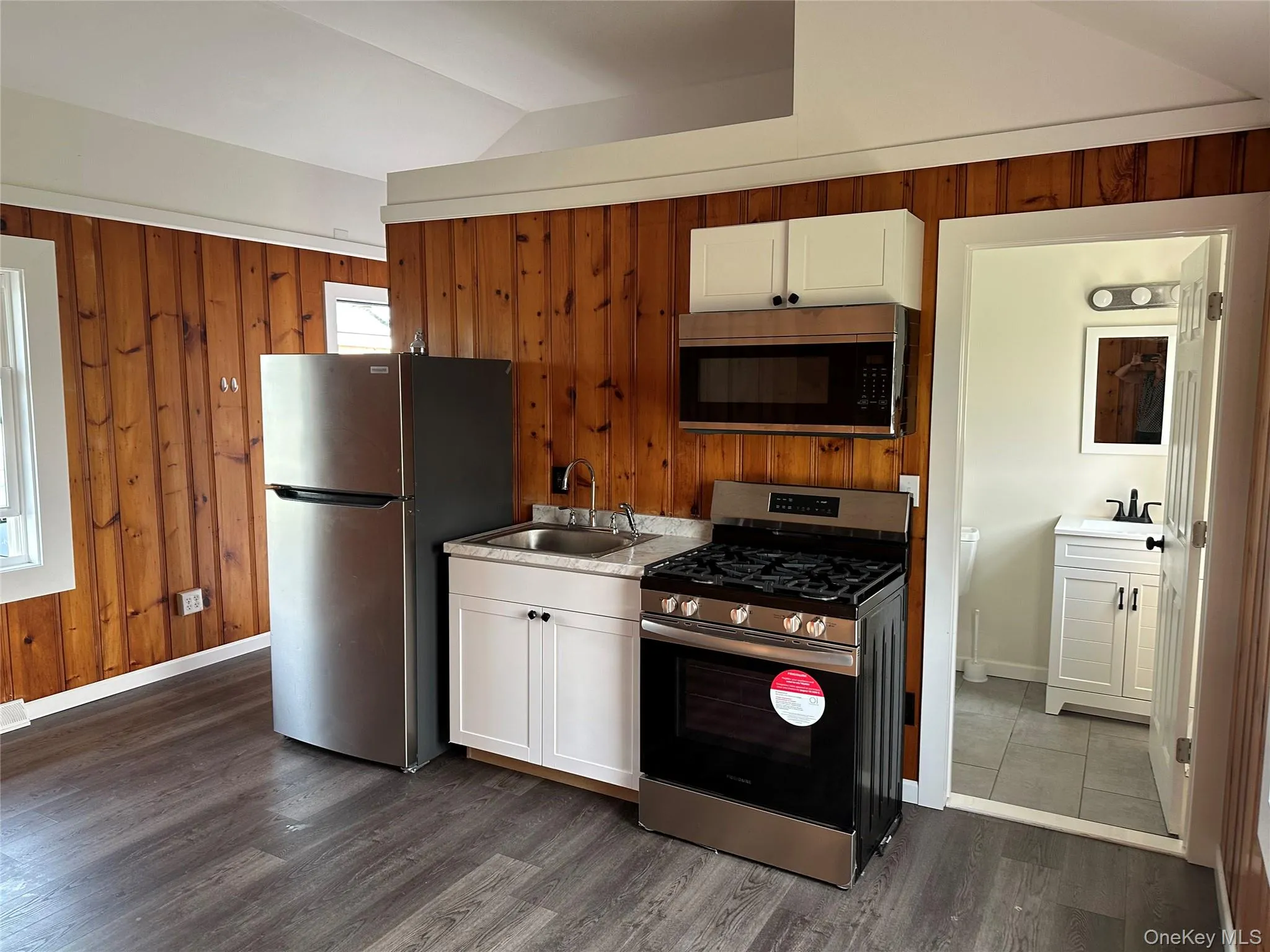 Compact kitchen area featuring stainless steel appliances, white cabinetry, a built-in microwave, and wood-finish flooring Compact kitchen area featuring stainless steel appliances, white cabinetry, a built-in microwave, and wood-finish flooring