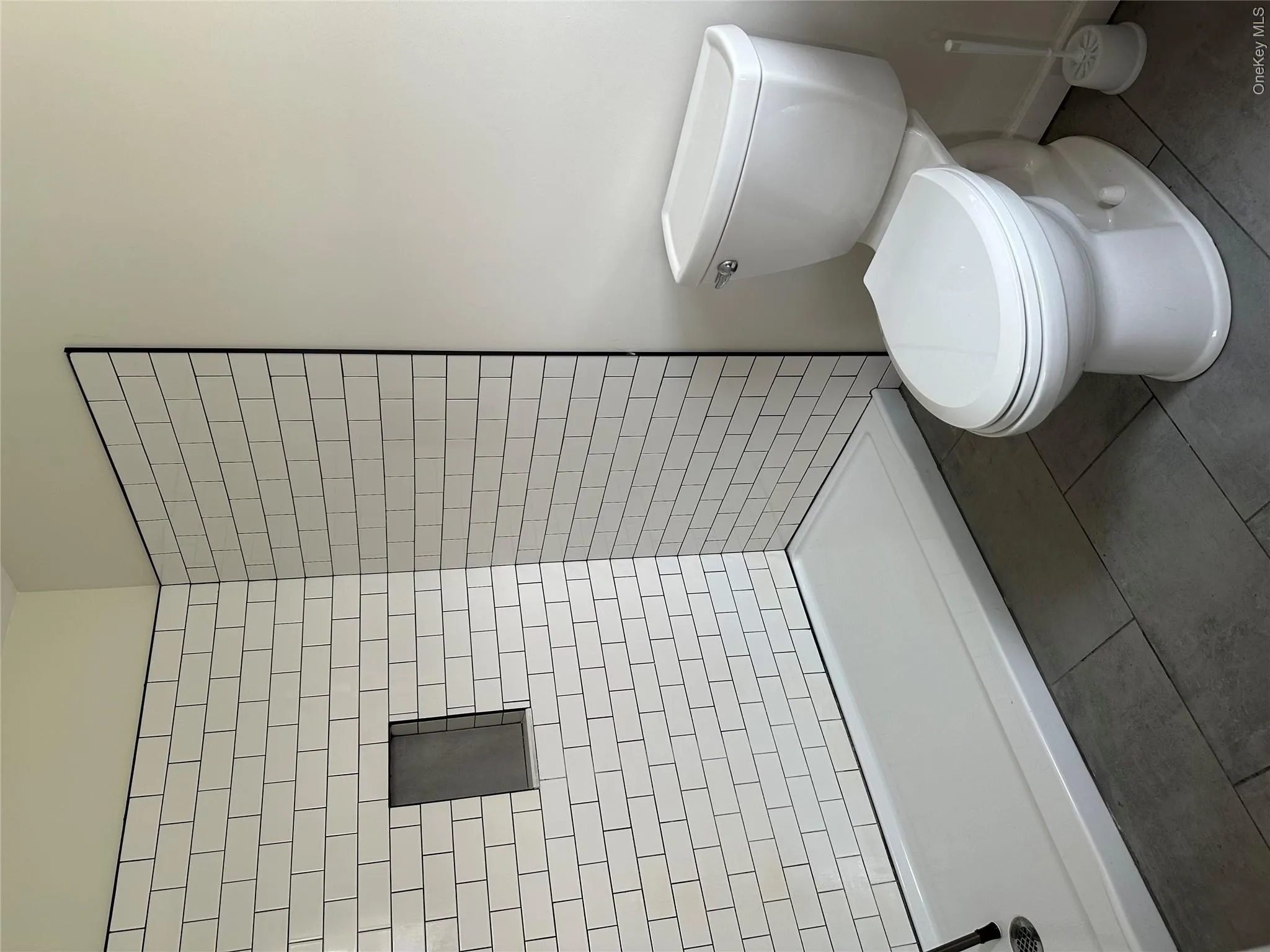 Bathroom featuring a subway tile shower with a built-in niche, a white shower pan, and dark gray tile flooring Bathroom featuring a subway tile shower with a built-in niche, a white shower pan, and dark gray tile flooring