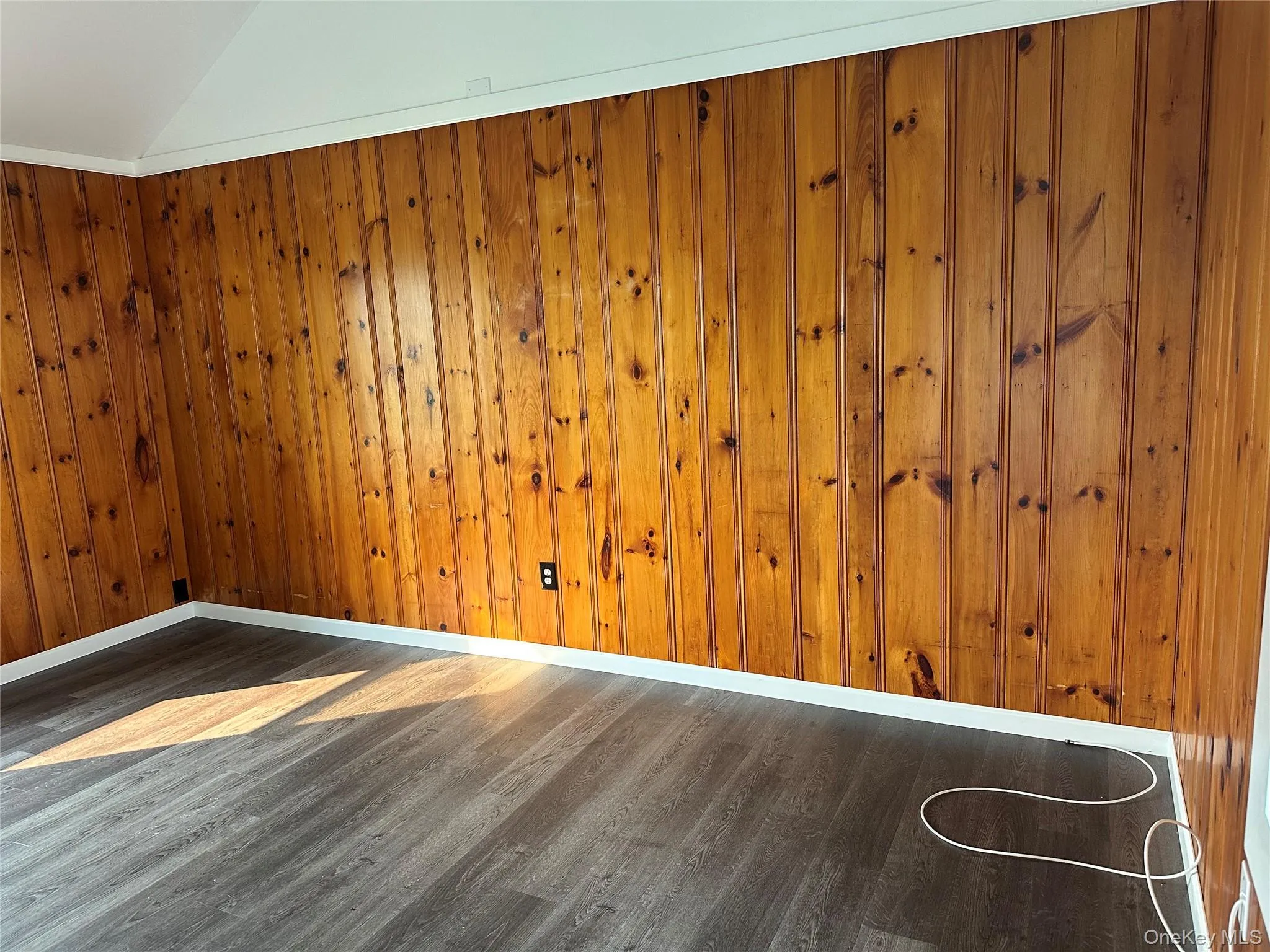 Wood-paneled wall with white trim and dark wood-finish flooring Wood-paneled wall with white trim and dark wood-finish flooring