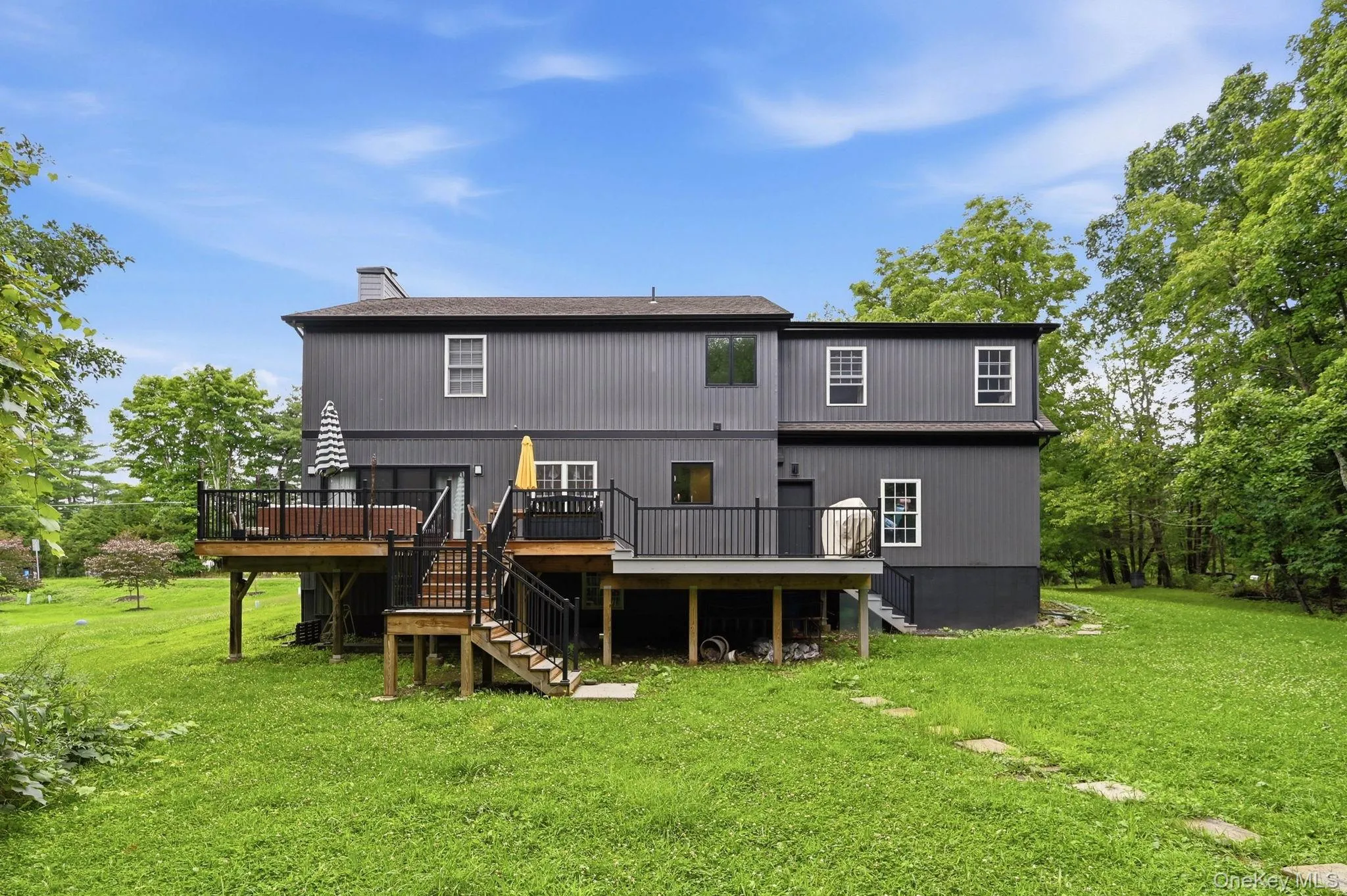 Rear exterior featuring a multi-level wood deck with black railings, a walk-out lower level, and a expansive grassy yard Rear exterior featuring a multi-level wood deck with black railings, a walk-out lower level, and a expansive grassy yard