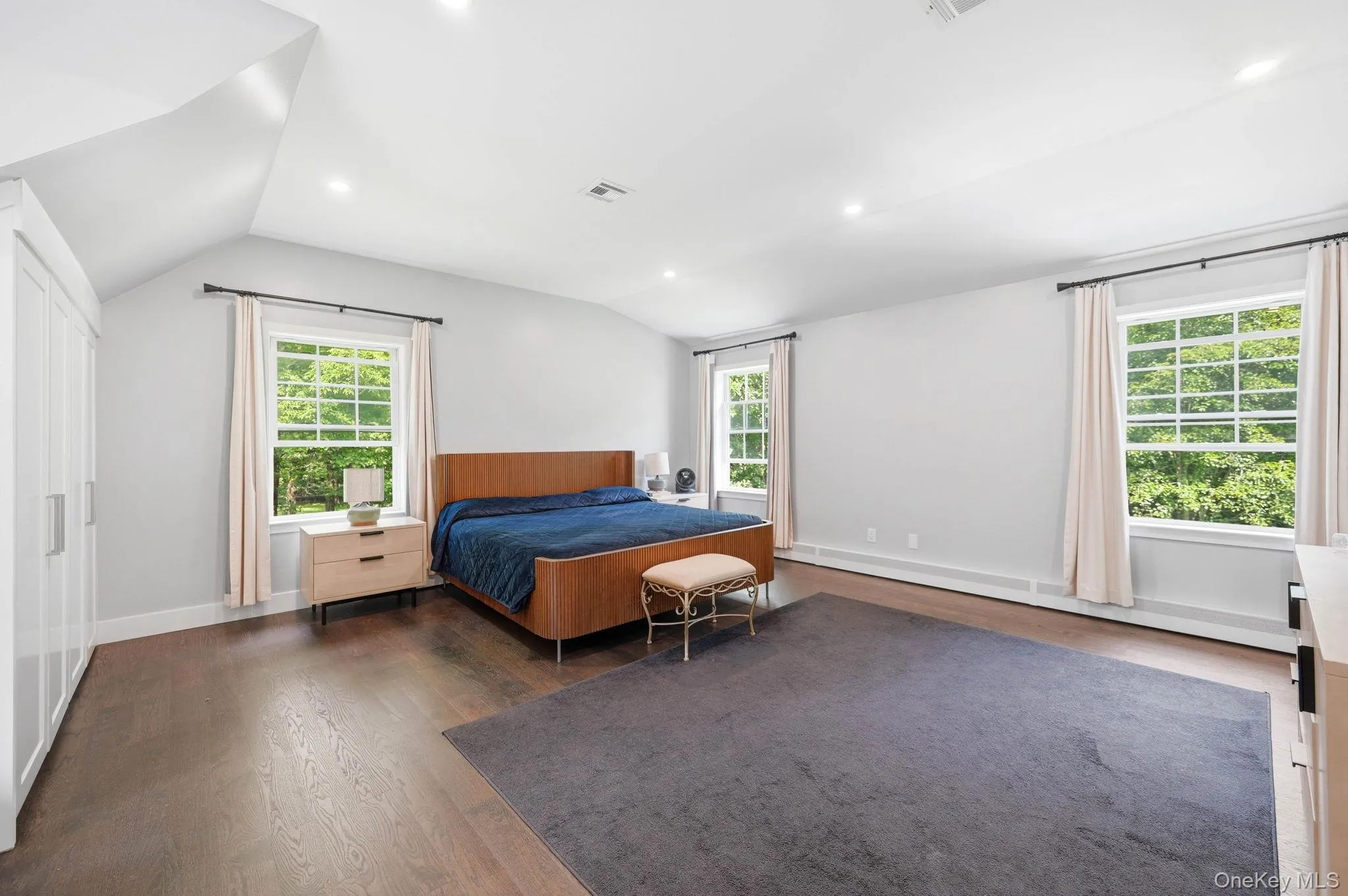Spacious room featuring rich wood-finish flooring, white walls, and a vaulted ceiling with recessed lighting Spacious room featuring rich wood-finish flooring, white walls, and a vaulted ceiling with recessed lighting