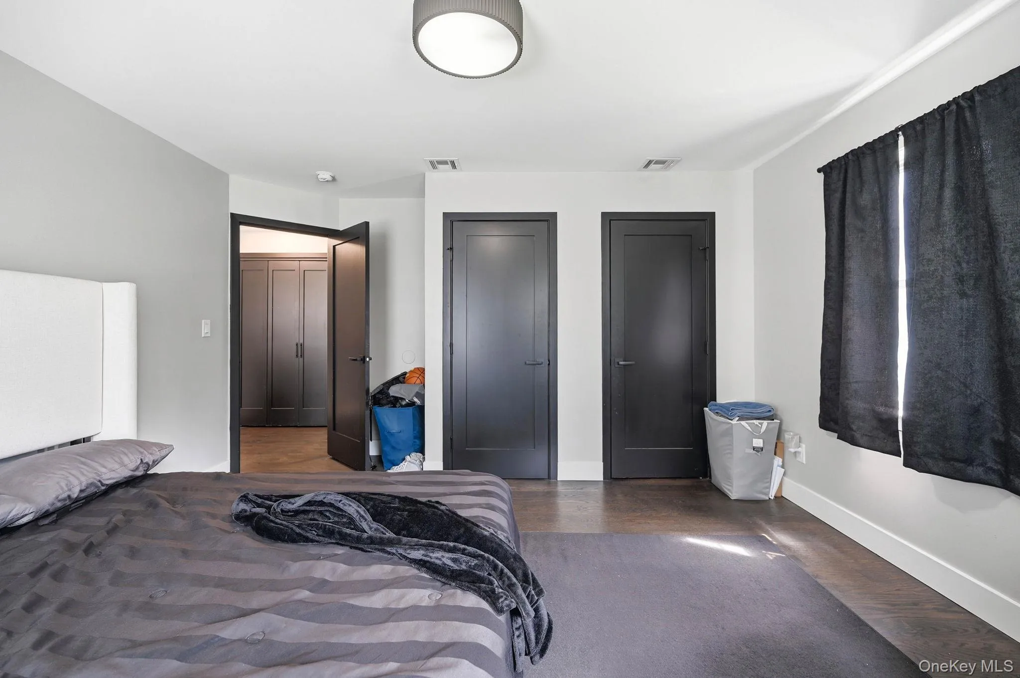 Spacious room featuring dark wood-finish flooring, light grey walls, and white baseboards Spacious room featuring dark wood-finish flooring, light grey walls, and white baseboards