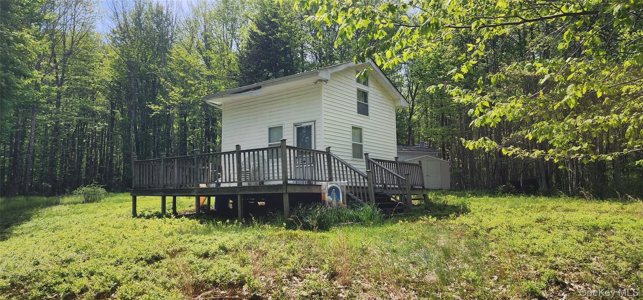 View of home's exterior with a storage unit, a wooden deck, an outdoor structure, and a view of trees View of home's exterior with a storage unit, a wooden deck, an outdoor structure, and a view of trees