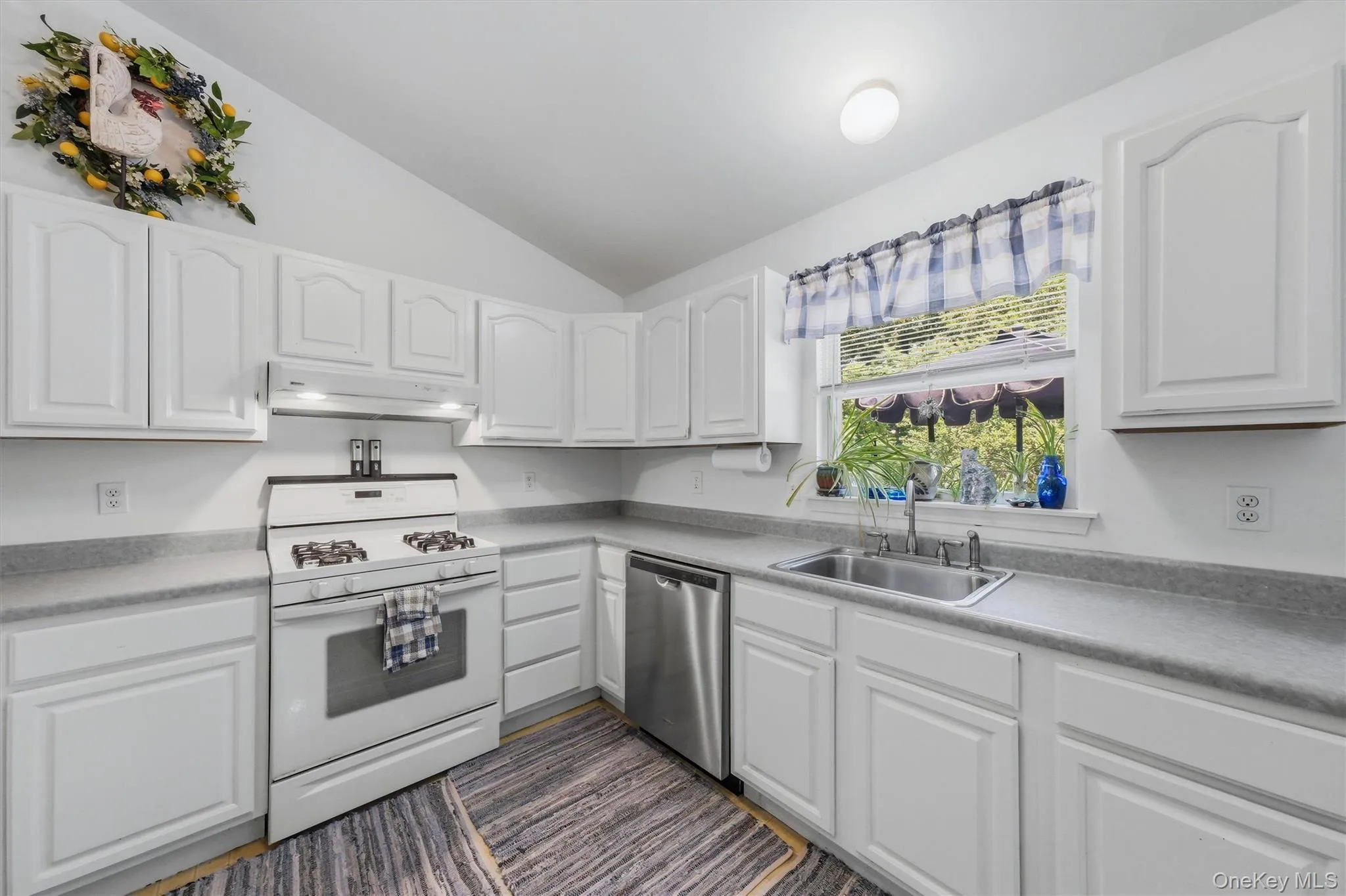 White cabinetry, gas range, stainless steel dishwasher, double basin sink, and a vaulted ceiling White cabinetry, gas range, stainless steel dishwasher, double basin sink, and a vaulted ceiling