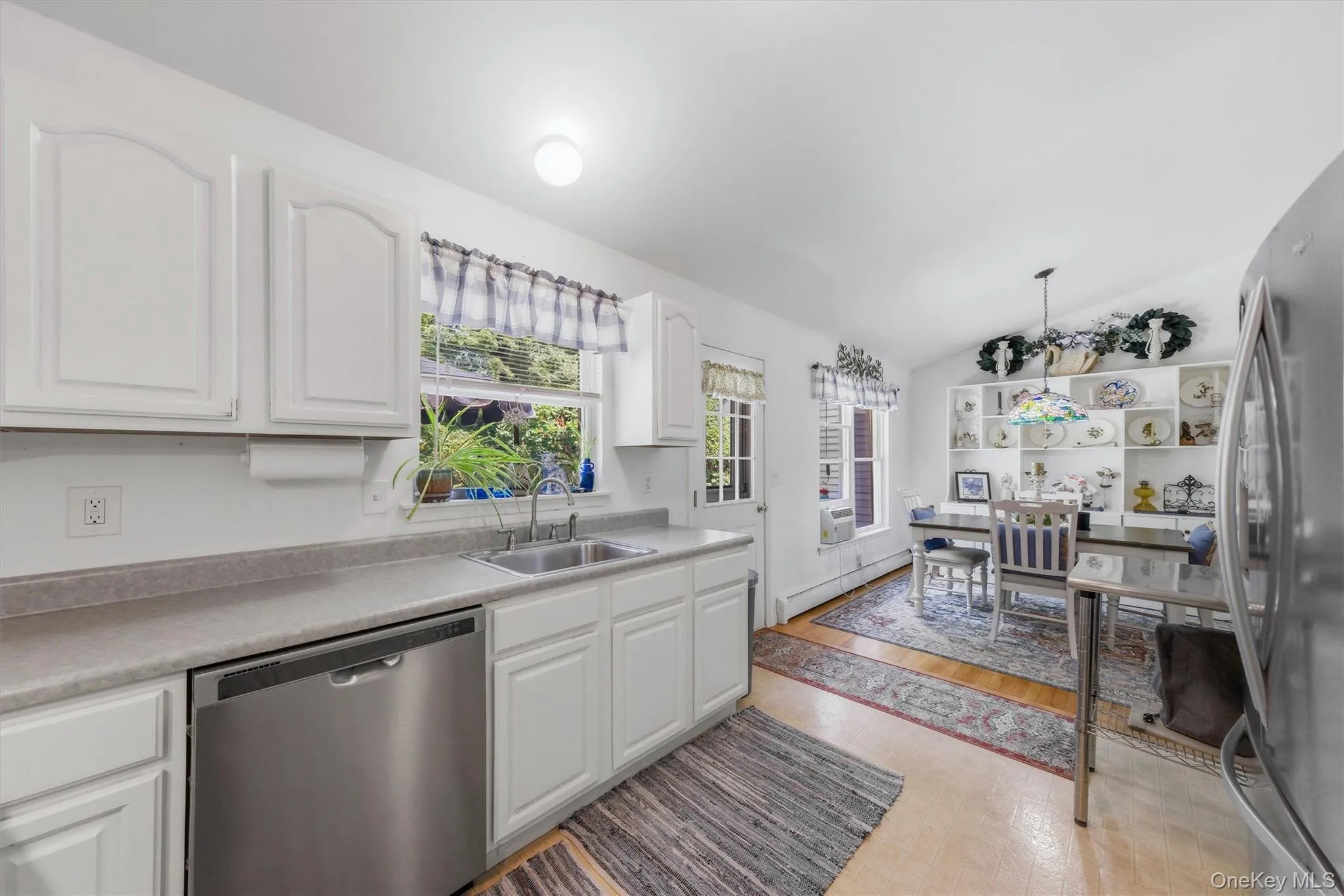 White cabinetry, stainless steel dishwasher, dual basin sink, light-toned countertops, and wood-finish flooring White cabinetry, stainless steel dishwasher, dual basin sink, light-toned countertops, and wood-finish flooring