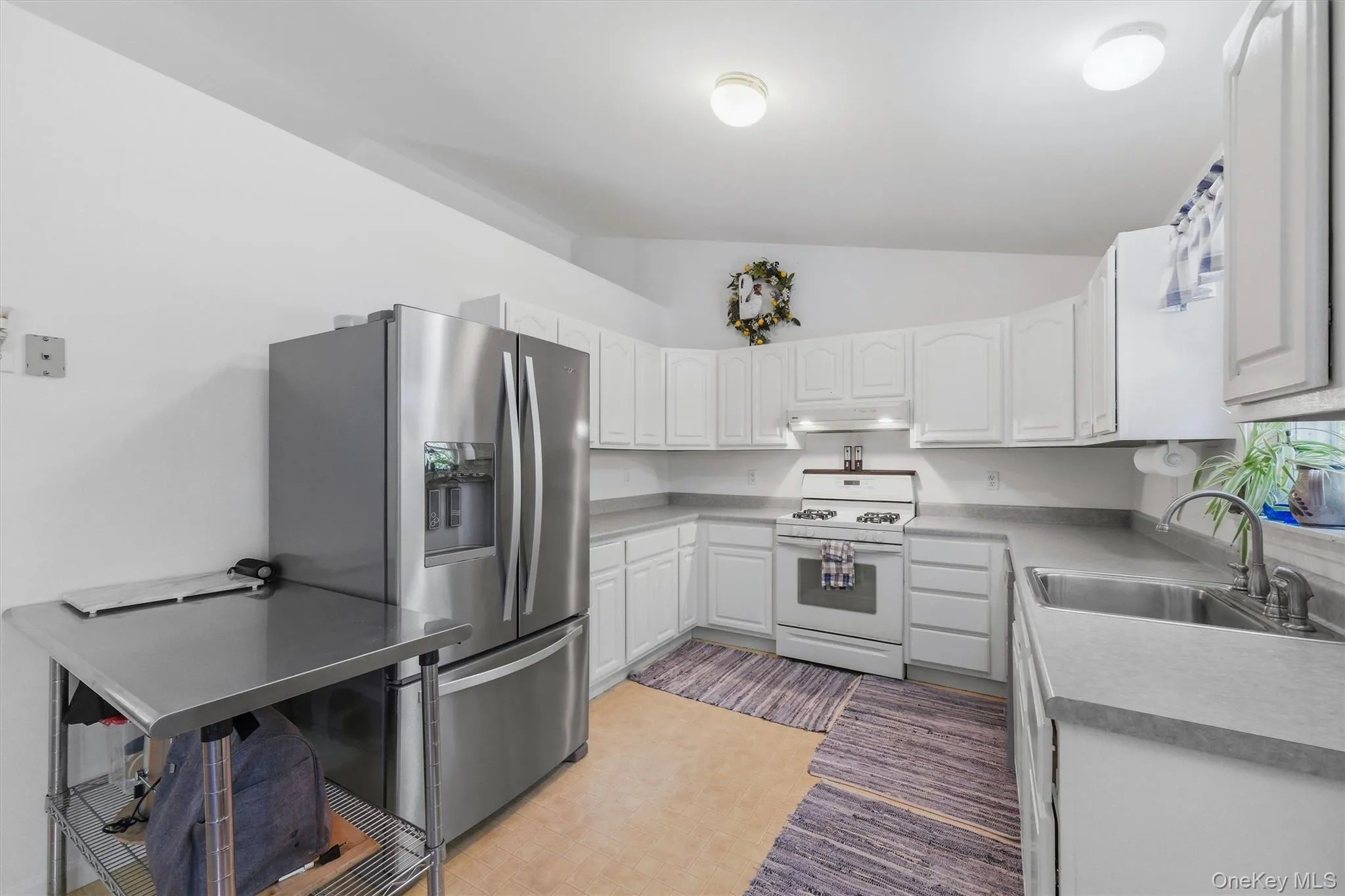 Stainless steel French door refrigerator, white cabinetry, light-toned countertops, stainless steel sink, and a white range Stainless steel French door refrigerator, white cabinetry, light-toned countertops, stainless steel sink, and a white range
