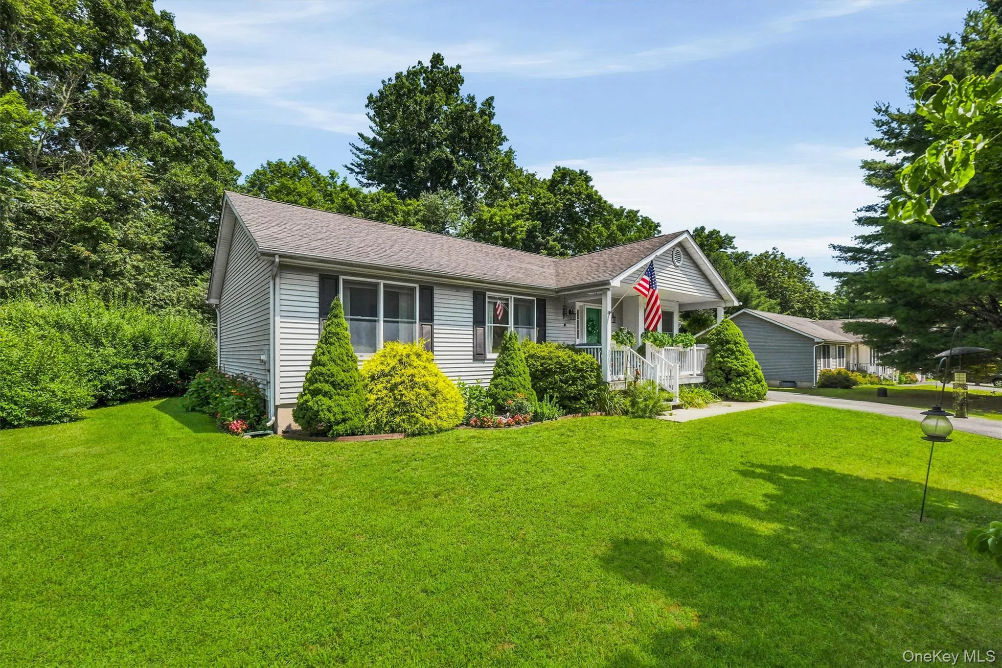 Expansive front lawn with mature landscaping, a charming covered porch, and white siding Expansive front lawn with mature landscaping, a charming covered porch, and white siding