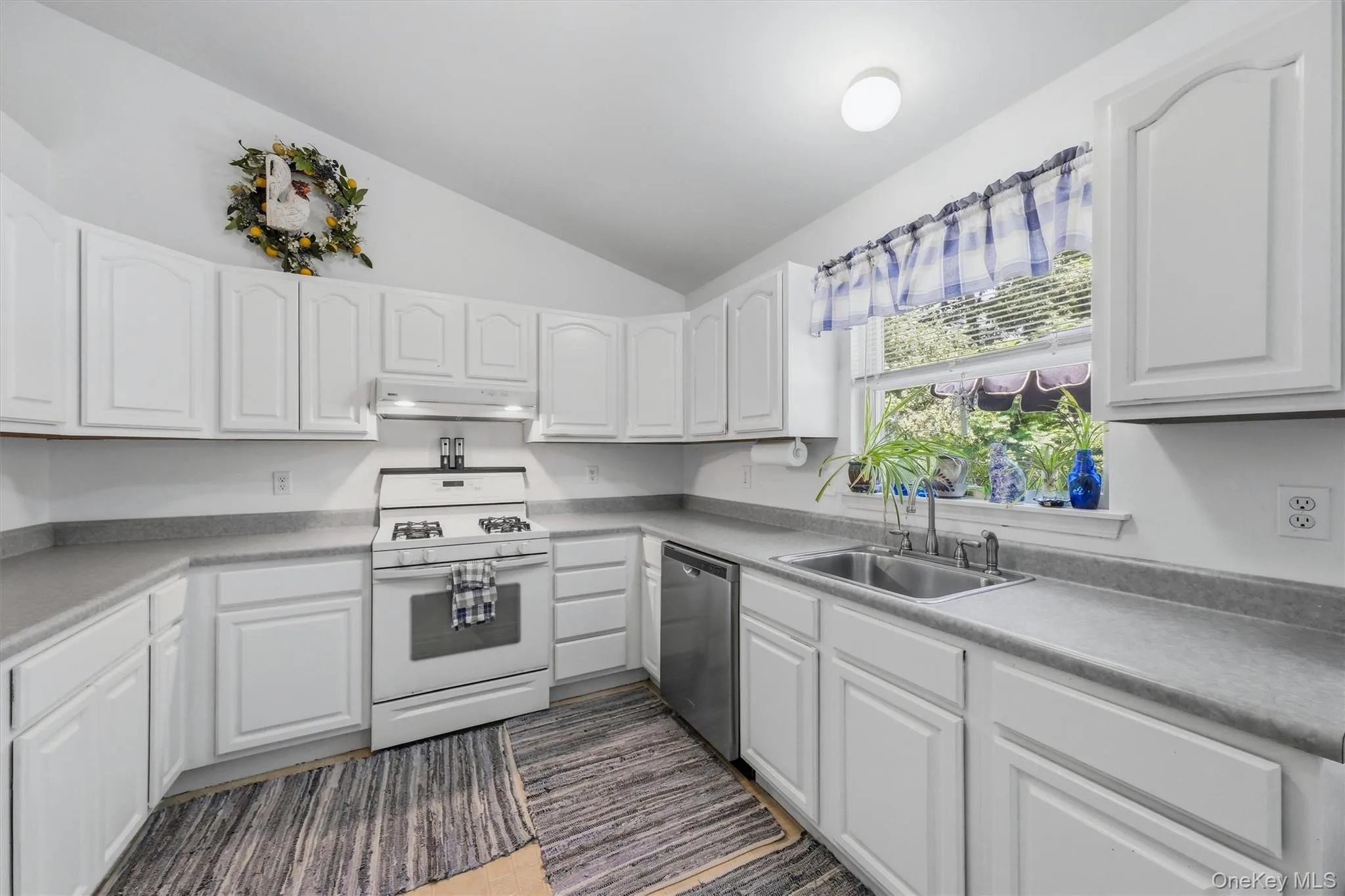 Kitchen featuring white cabinetry, light countertops, stainless steel sink, and a window Kitchen featuring white cabinetry, light countertops, stainless steel sink, and a window