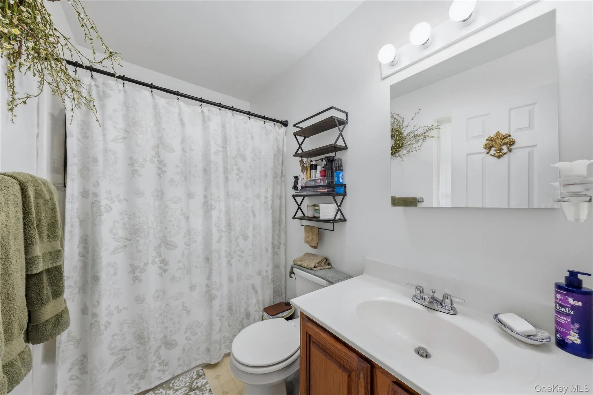 Vanity with an integrated sink and laminate countertop, framed mirror with vanity lighting, and wall-mounted shelving Vanity with an integrated sink and laminate countertop, framed mirror with vanity lighting, and wall-mounted shelving